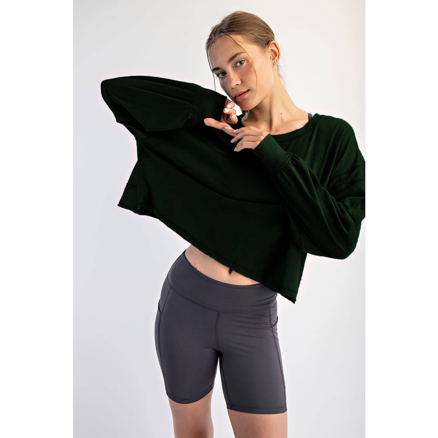 Woman wearing a dark green oversized sweater and gray shorts on a white background