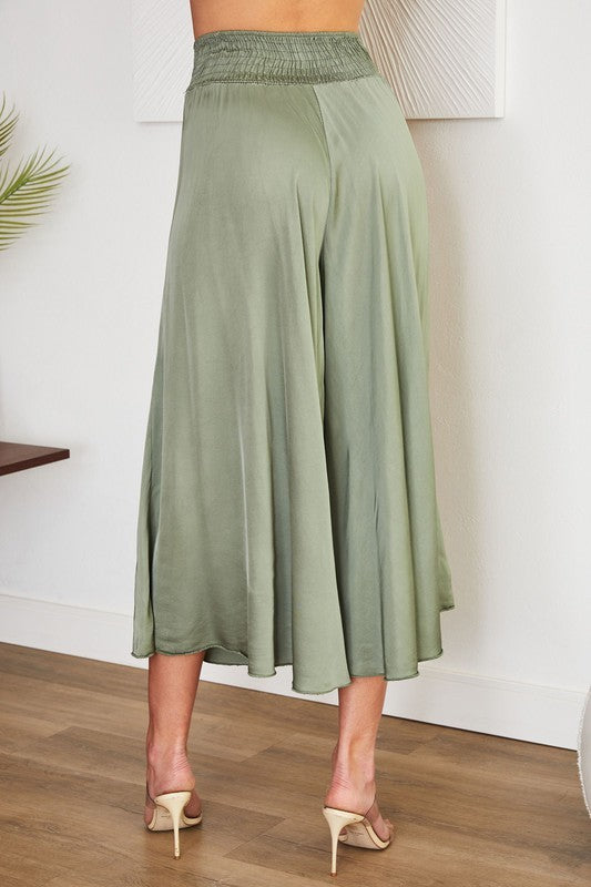 Green wide-leg pants worn by a person on a wooden floor with a white wall background