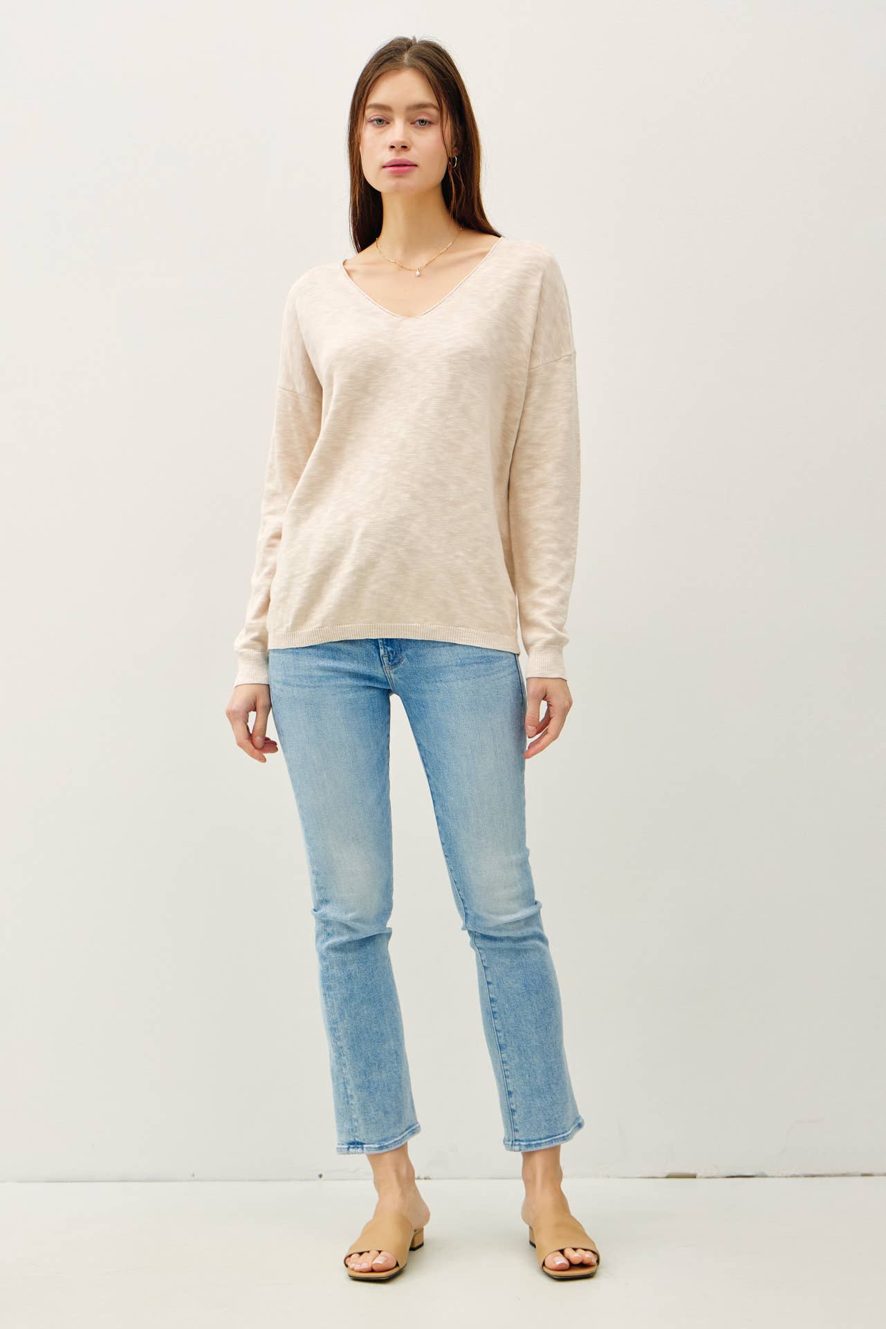 Woman wearing a beige sweater and light blue jeans on a white background