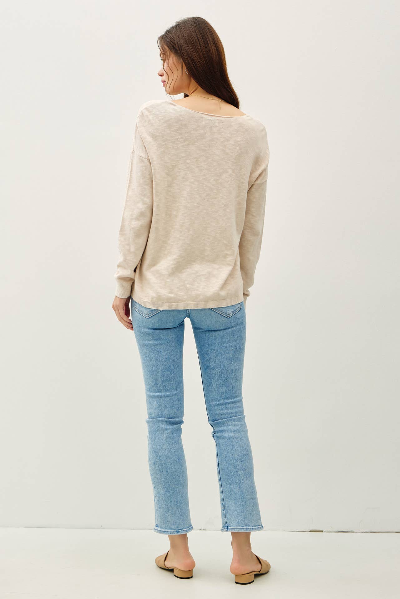 Woman wearing a beige sweater and light blue jeans on a white background