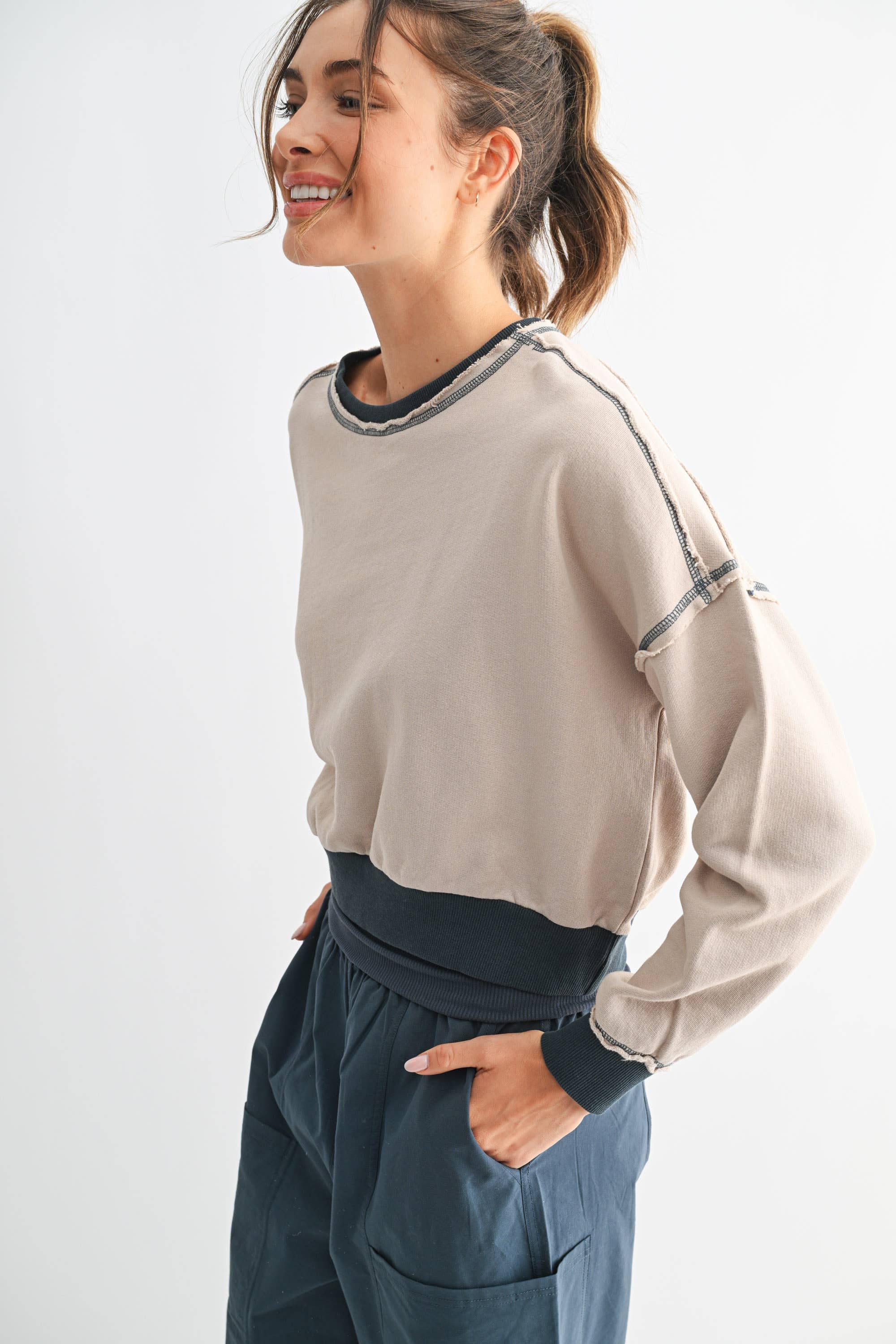 Woman wearing a beige long-sleeve top and blue pants on a white background
