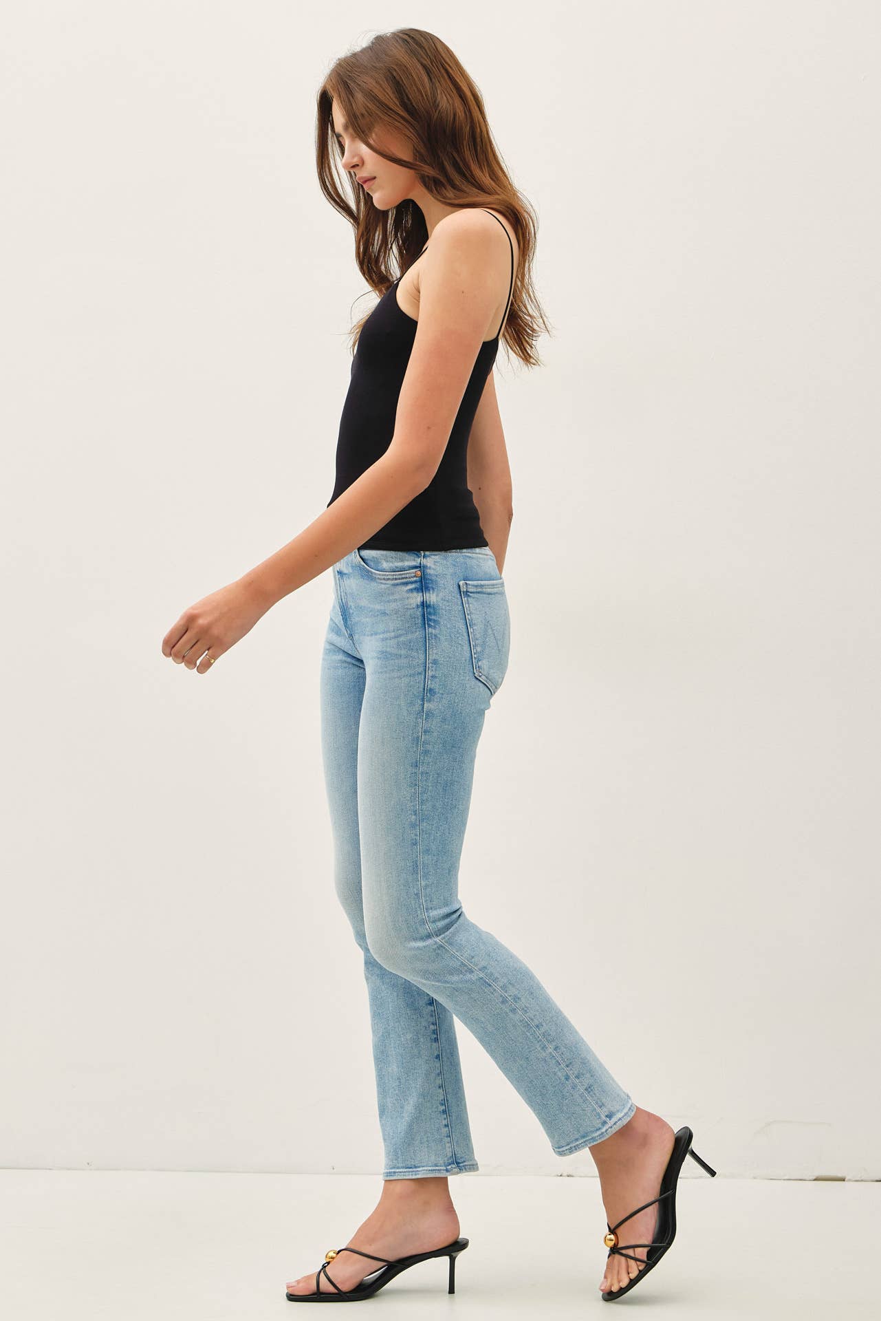 Woman wearing light blue jeans and a black top on a white background