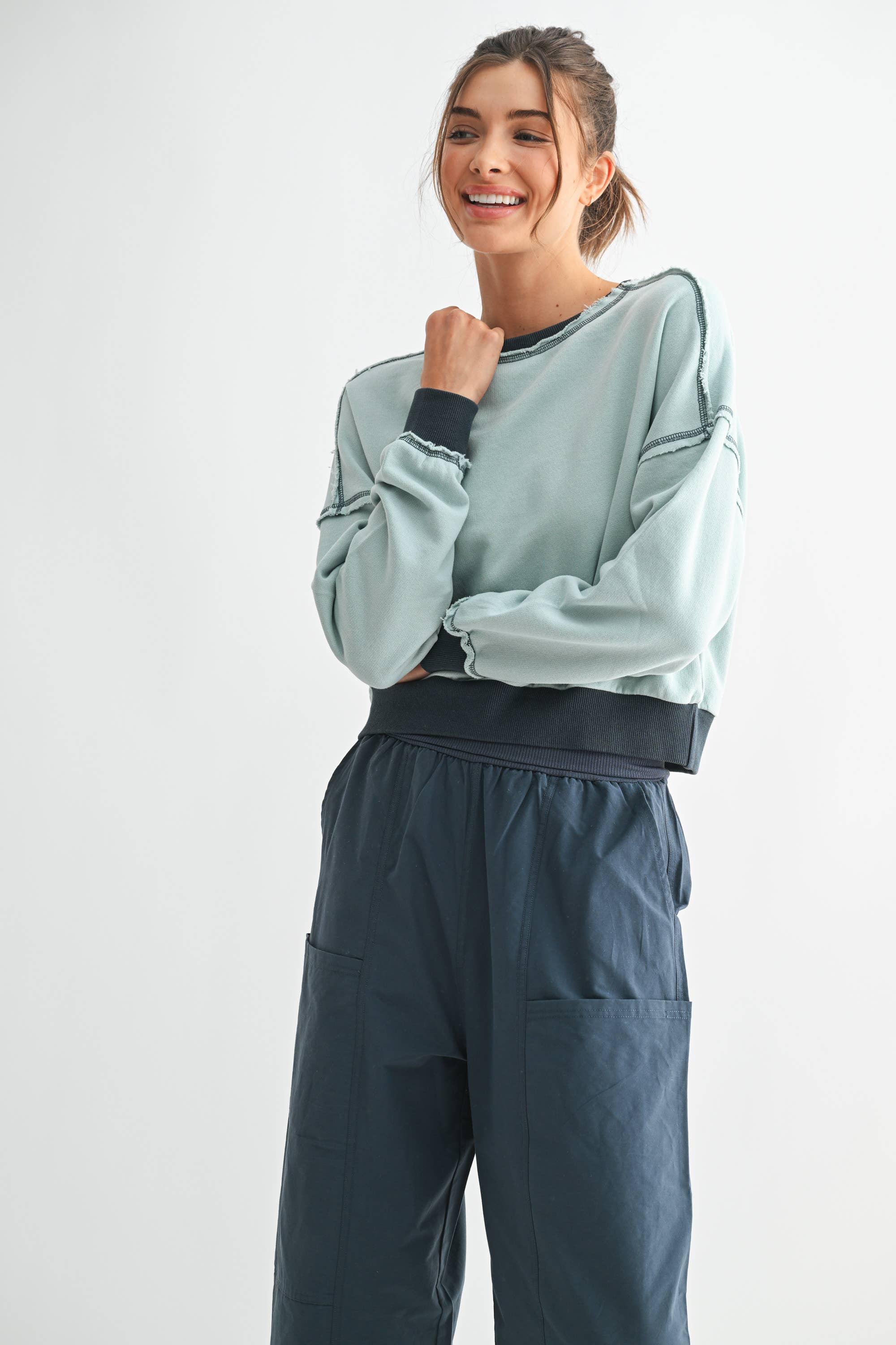 Woman wearing a light gray sweatshirt and dark gray pants on a white background
