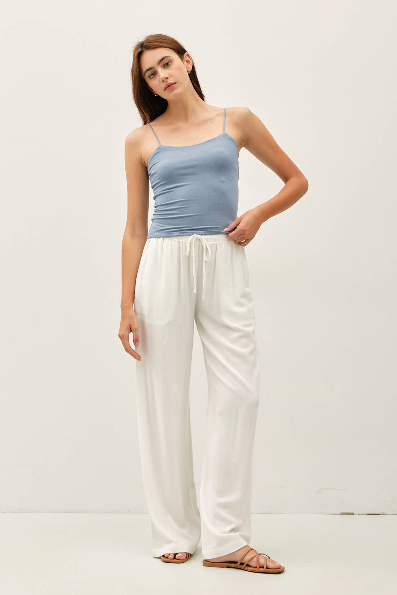 Woman wearing a blue top and white pants on a plain background