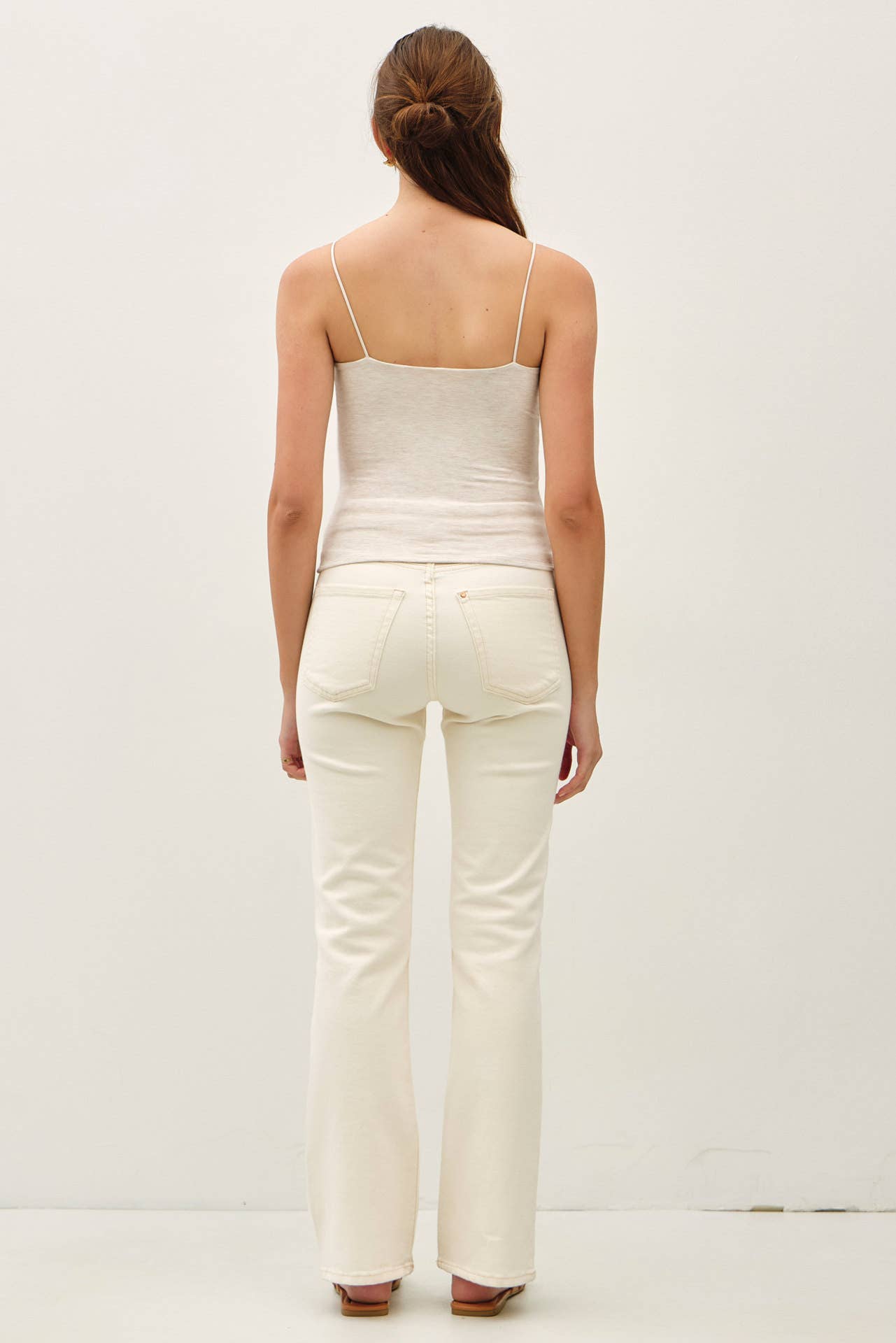 Woman wearing a oatmeal spaghetti strap top and pants on a plain background