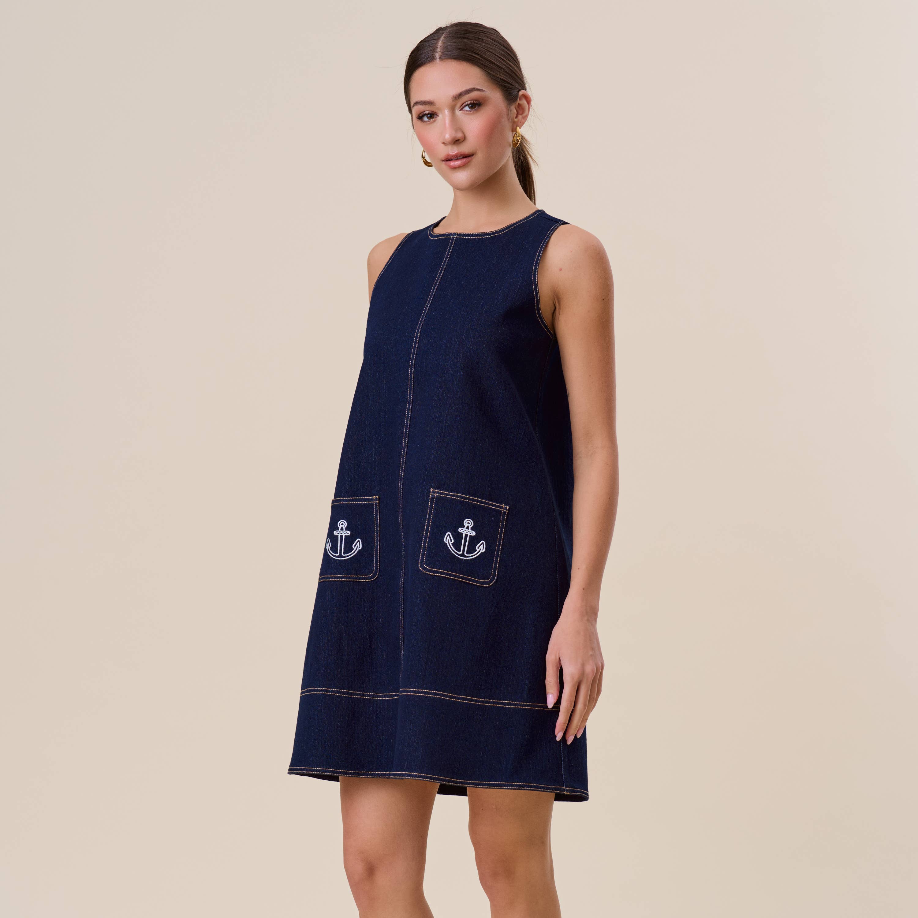 Woman wearing a navy dress with anchor pockets on a beige background