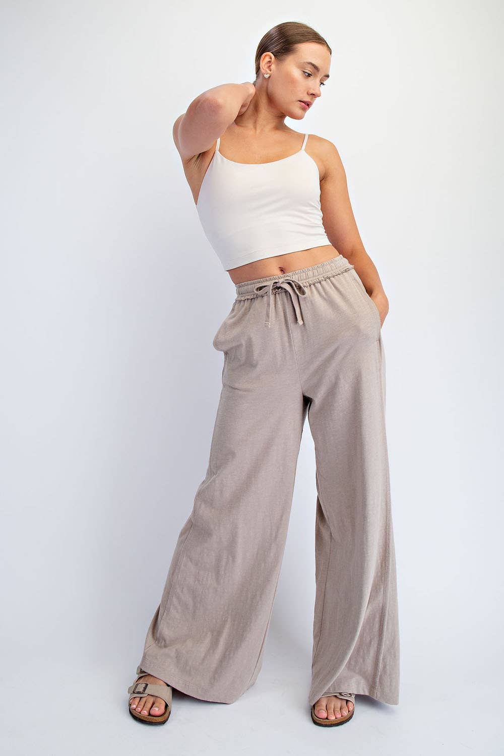 Woman wearing a white tank top and beige wide-leg pants on a white background