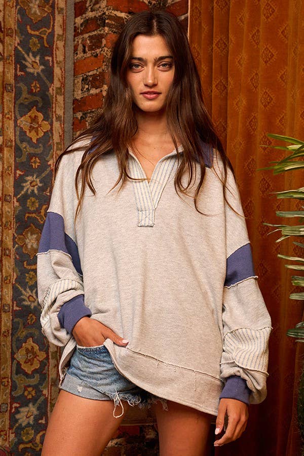 Woman wearing a beige sweater with blue sleeves and denim shorts in a patterned room.