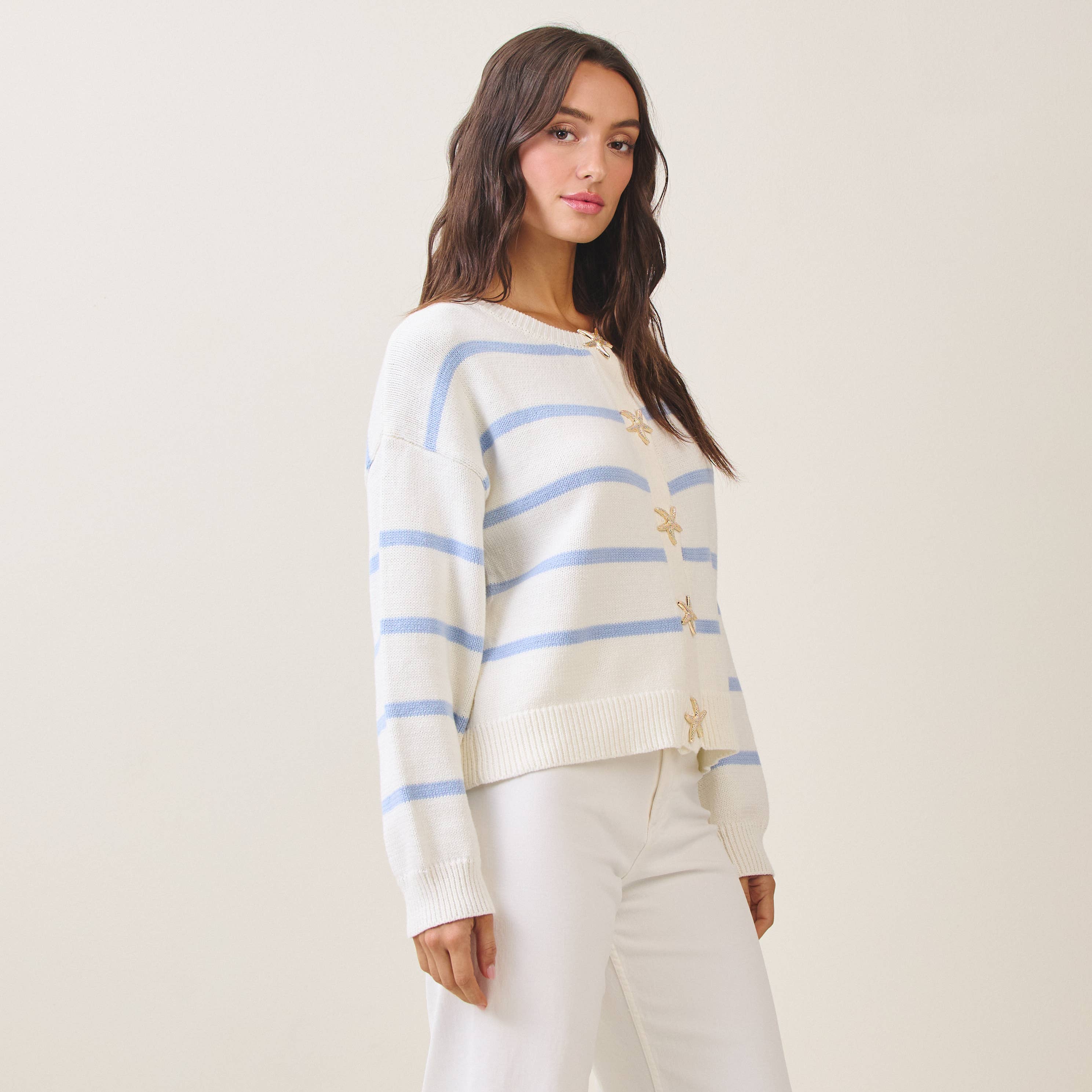 Woman wearing a cream sweater with blue stripes and gold accents on a plain background