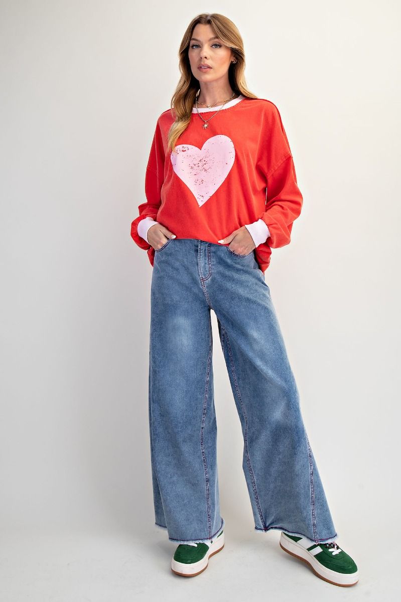 Woman wearing a red sweatshirt with a heart design and blue jeans on a white background