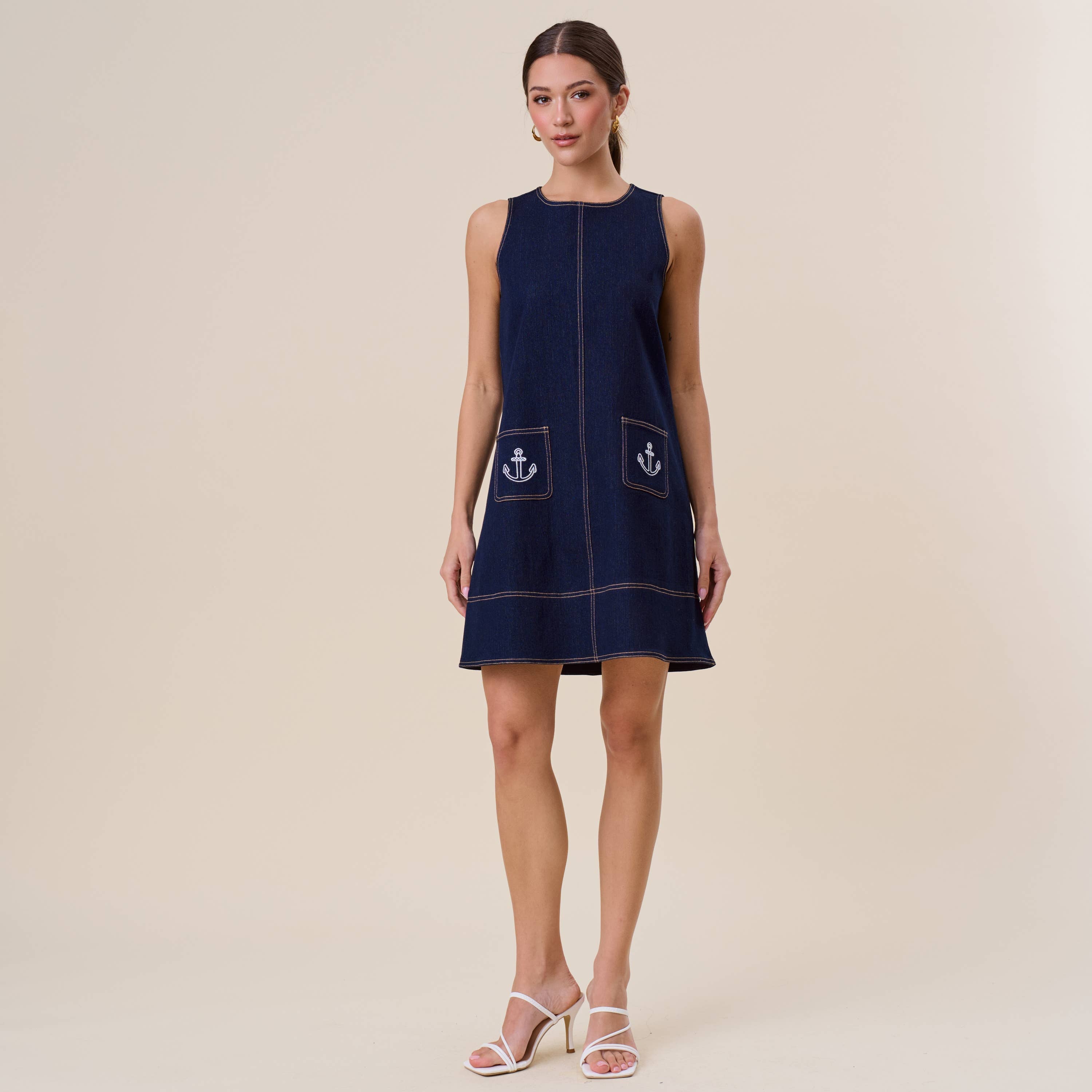 Woman wearing a navy sleeveless dress with anchor patterns on a beige background
