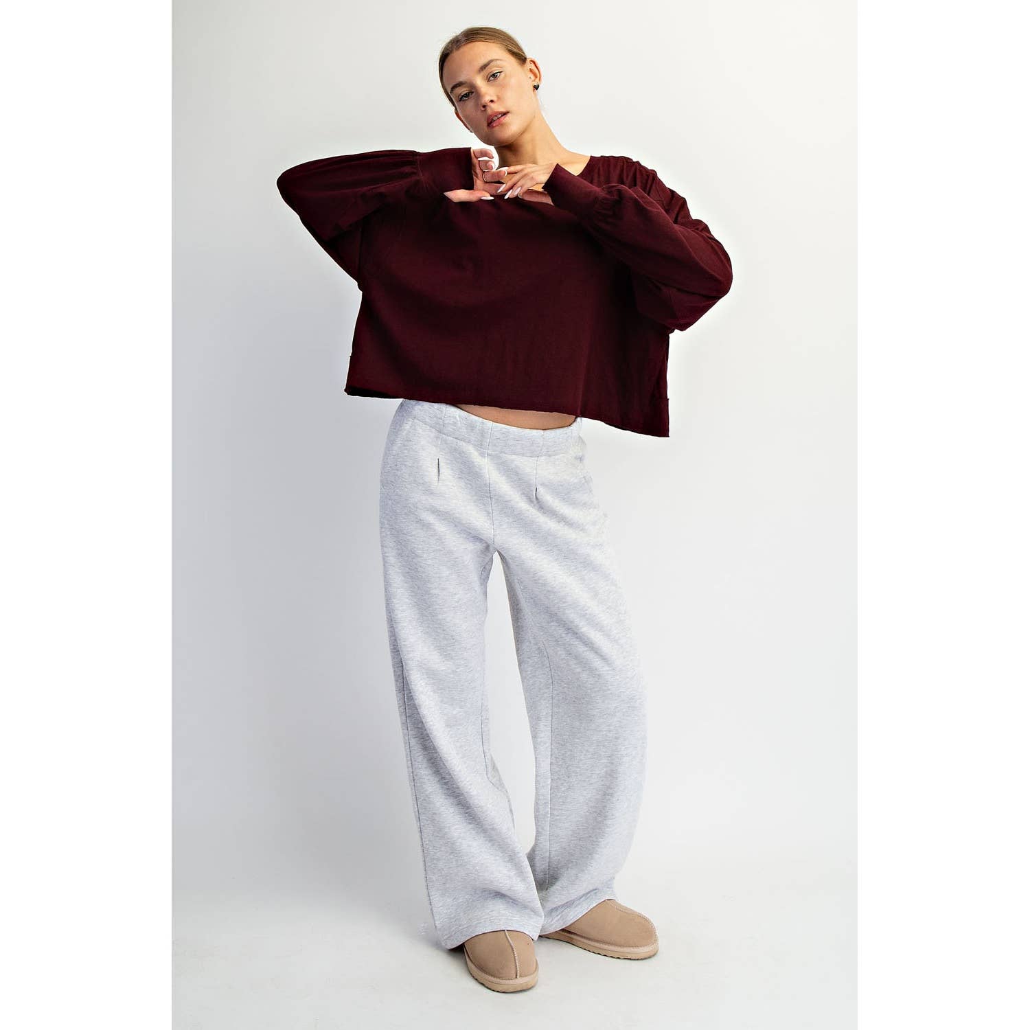 Person wearing a burgundy sweater and light gray pants on a white background