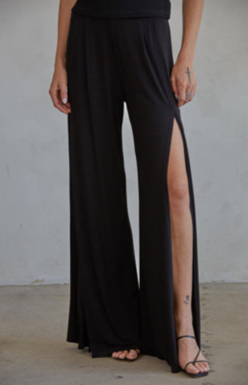 Black wide-leg pants with a high slit on a plain background