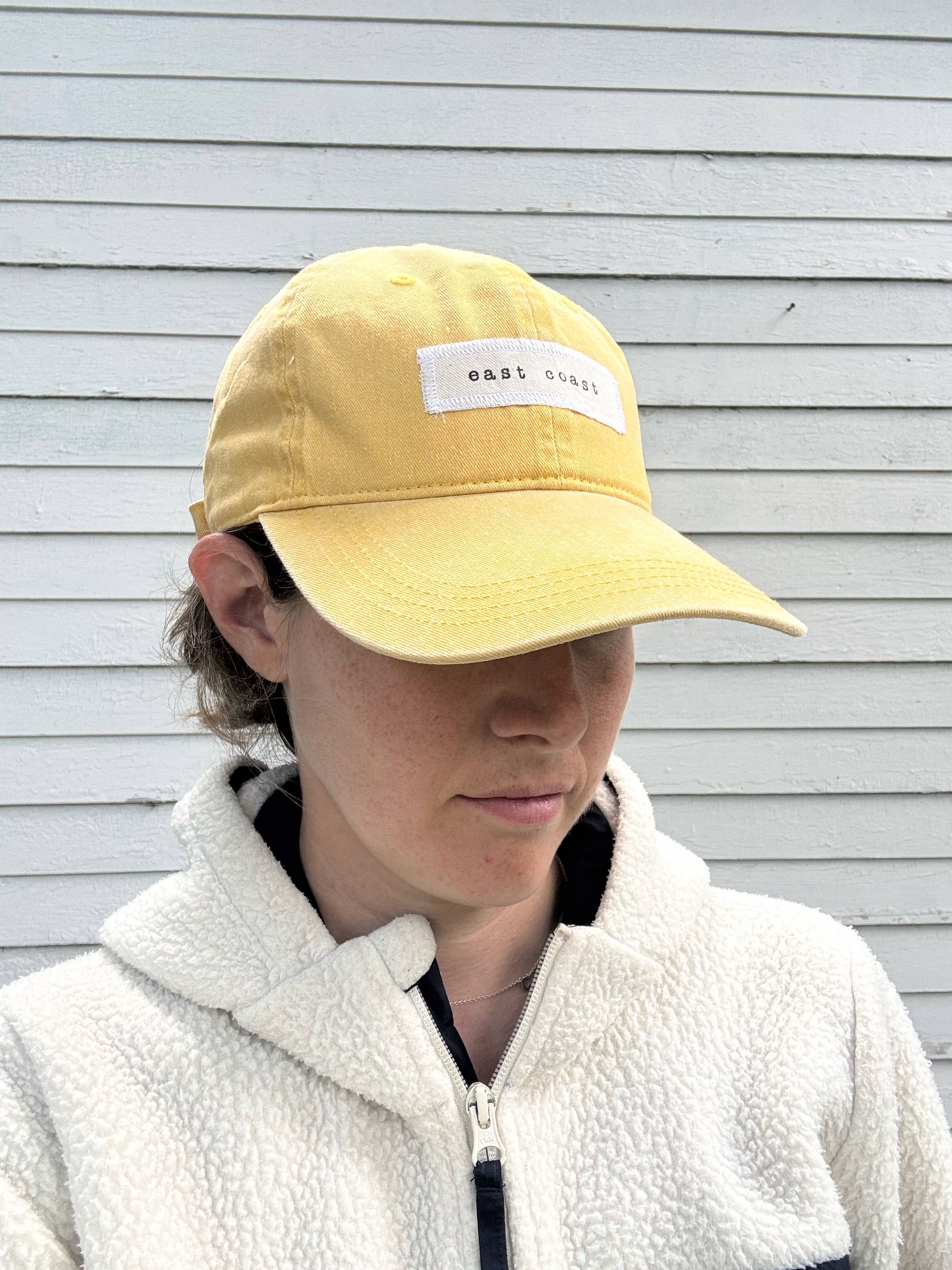 Person wearing a yellow cap with a logo against a light gray background