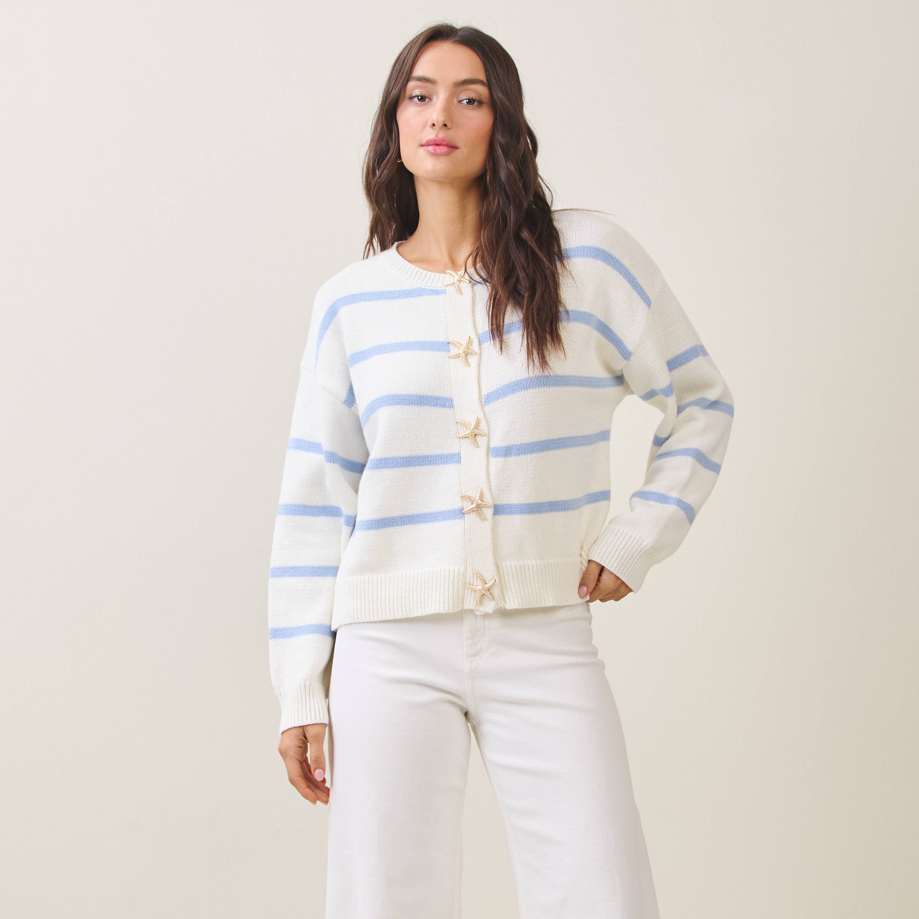 Woman wearing a white cardigan with blue stripes on a plain background