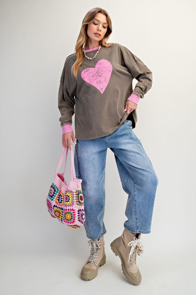 Woman wearing a gray sweatshirt with a pink heart design, blue jeans, and holding a colorful bag on a white background