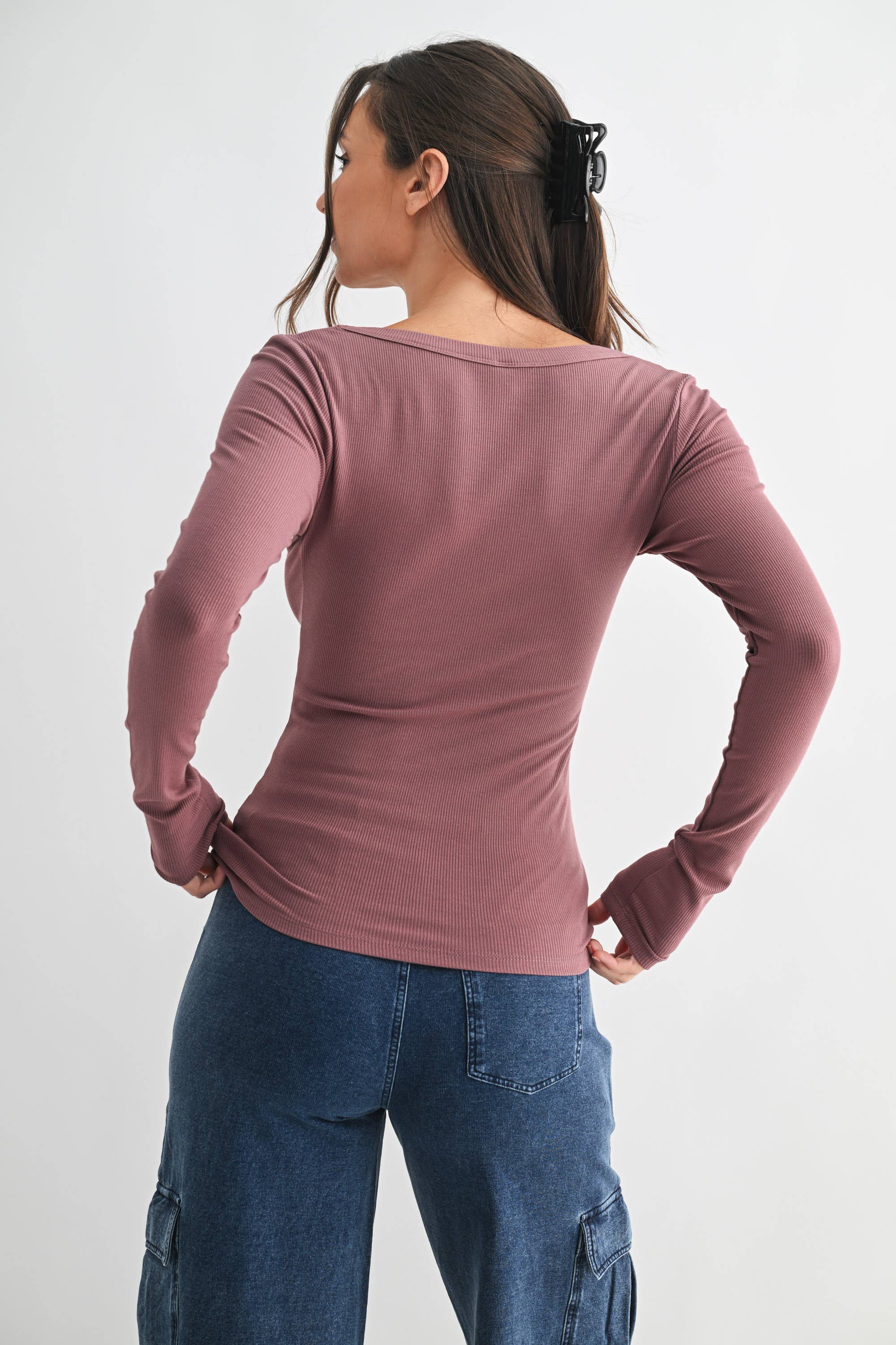 Woman wearing a mauve long-sleeve top and blue jeans on a white background