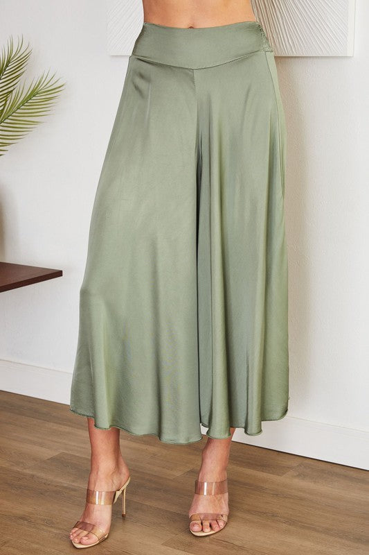 Green wide-leg pants worn by a person on a wooden floor with a white wall background
