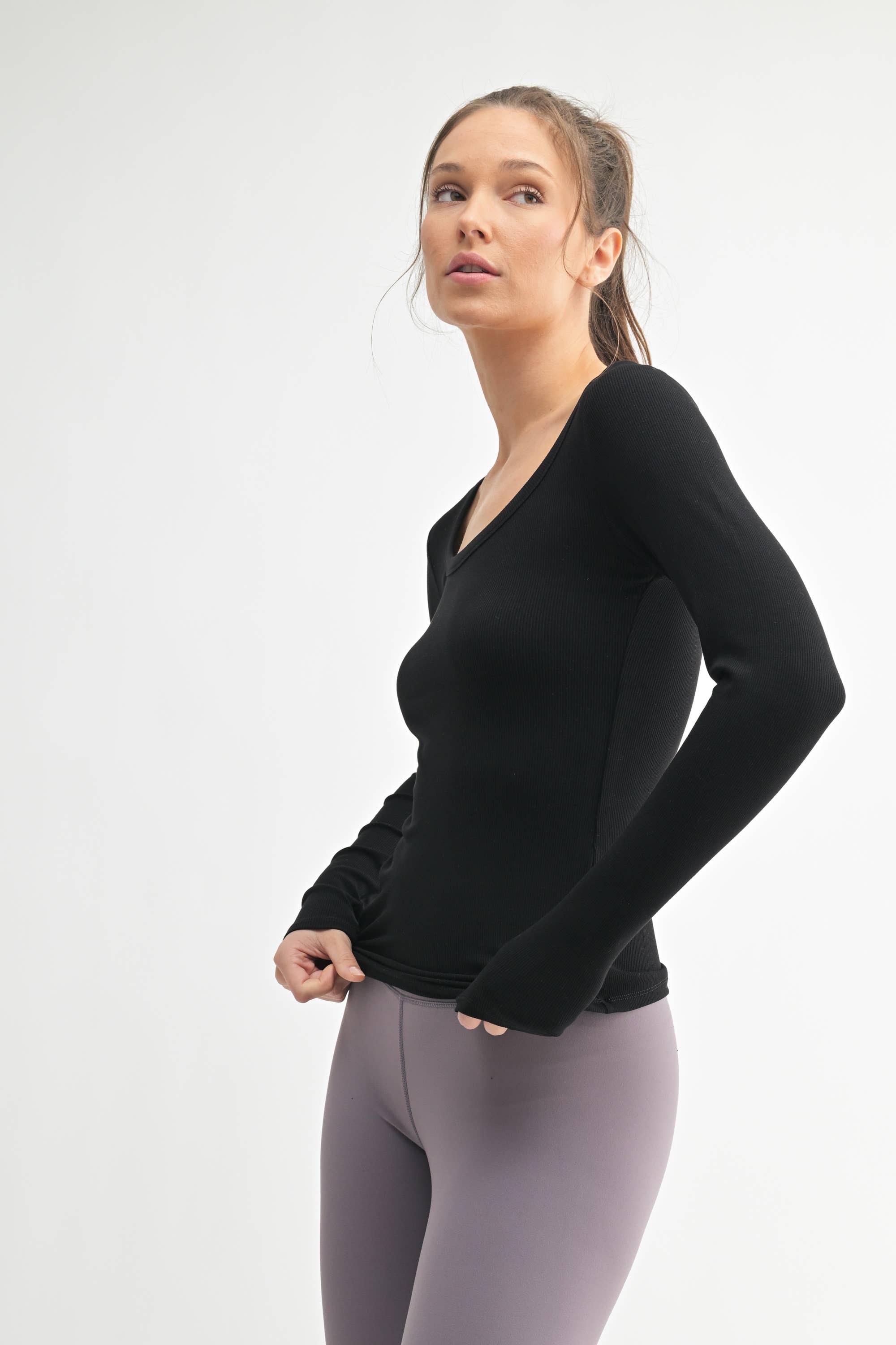 Woman wearing a black long-sleeve top and gray leggings on a white background