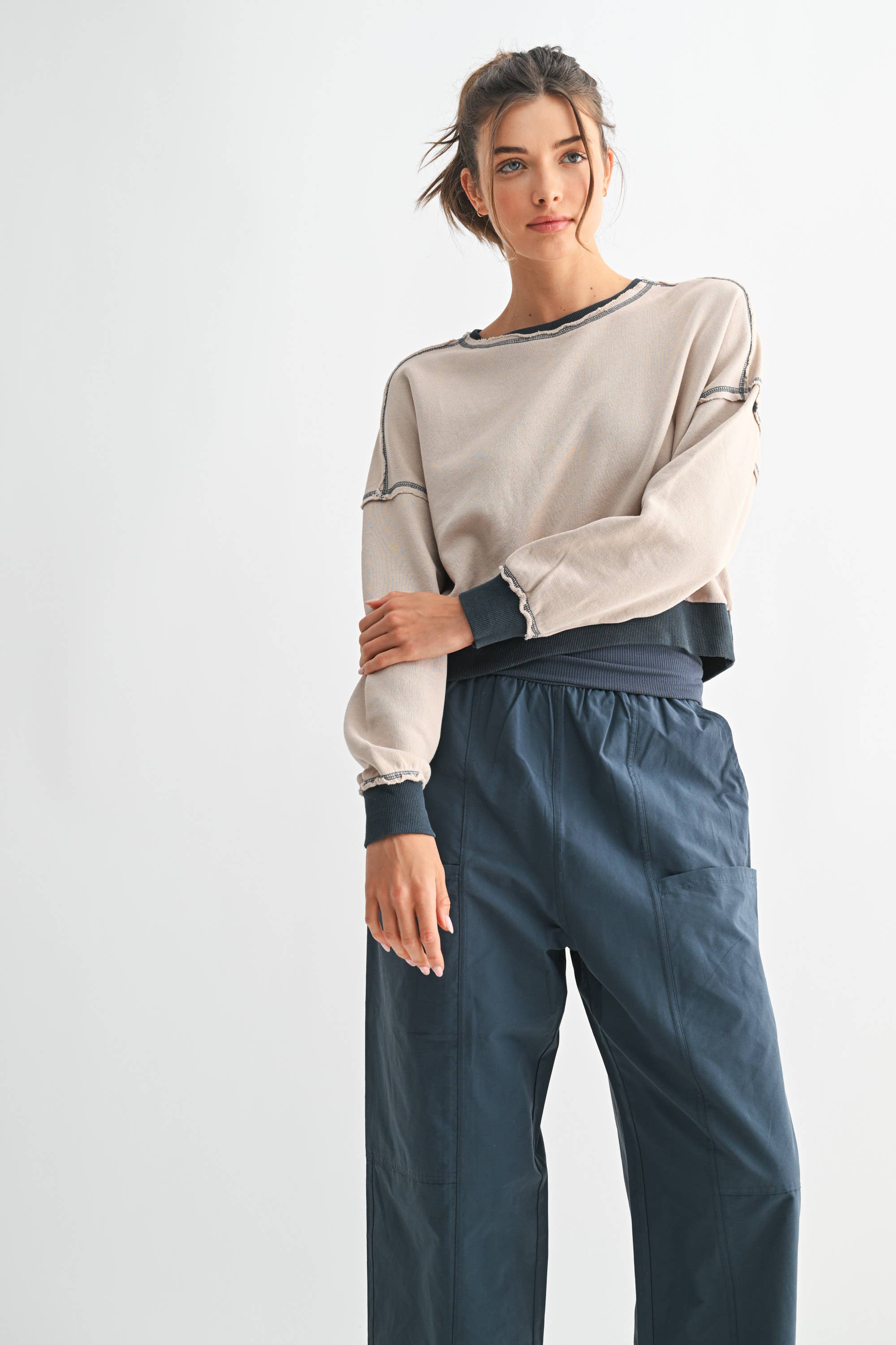 Woman wearing a beige long-sleeve top and dark blue pants on a white background