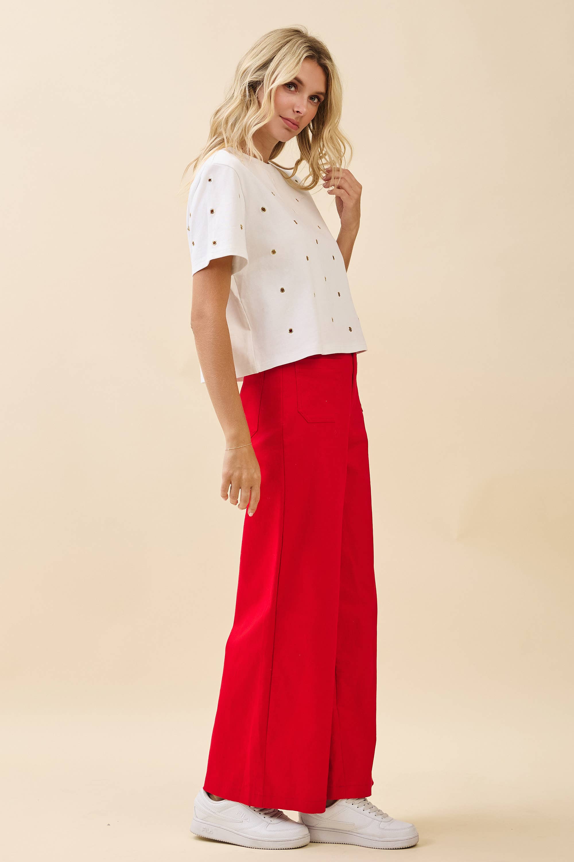 Woman wearing a white top with black polka dots and red pants on a beige background