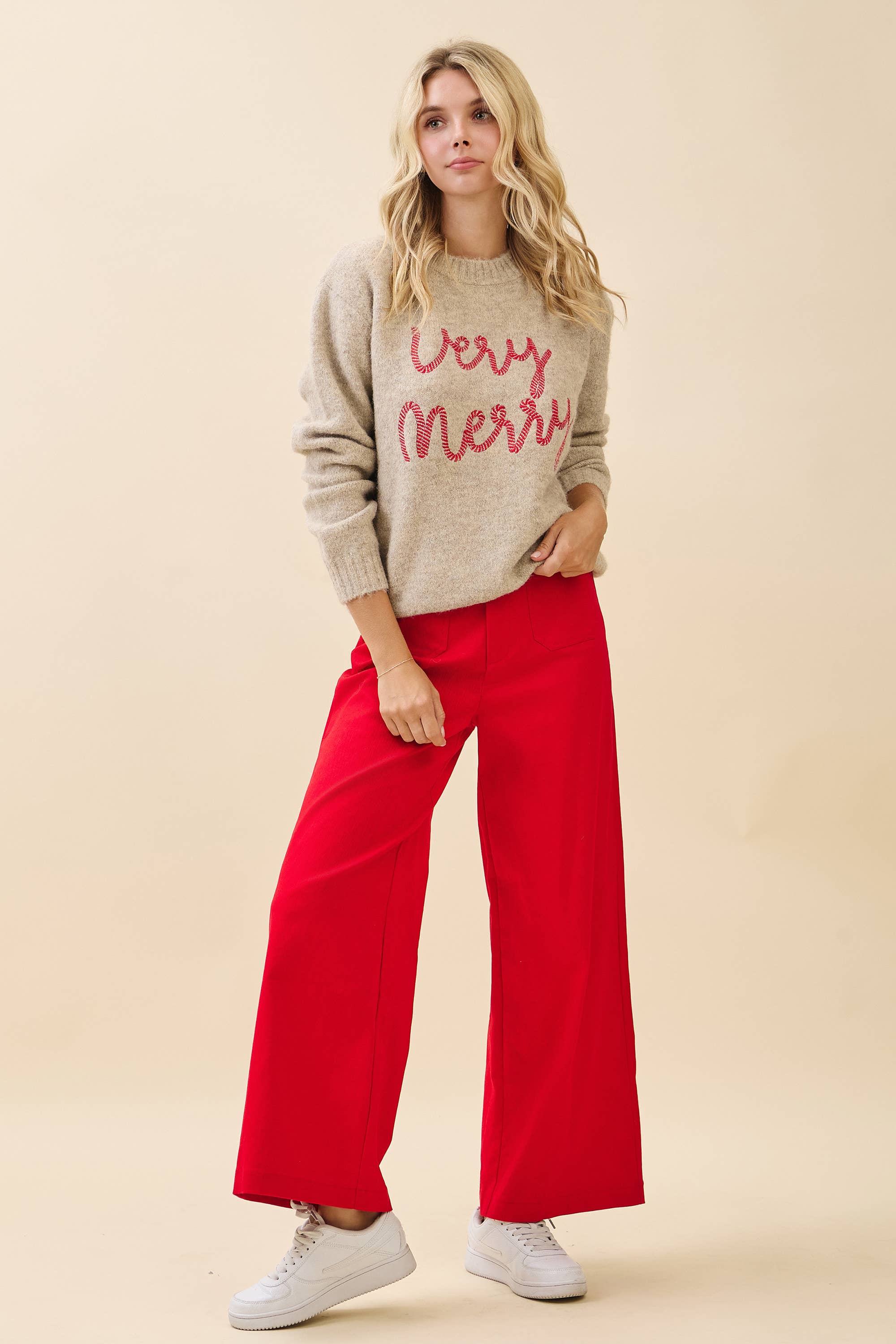 Woman wearing a 'Very Merry' sweater and red pants on a beige background