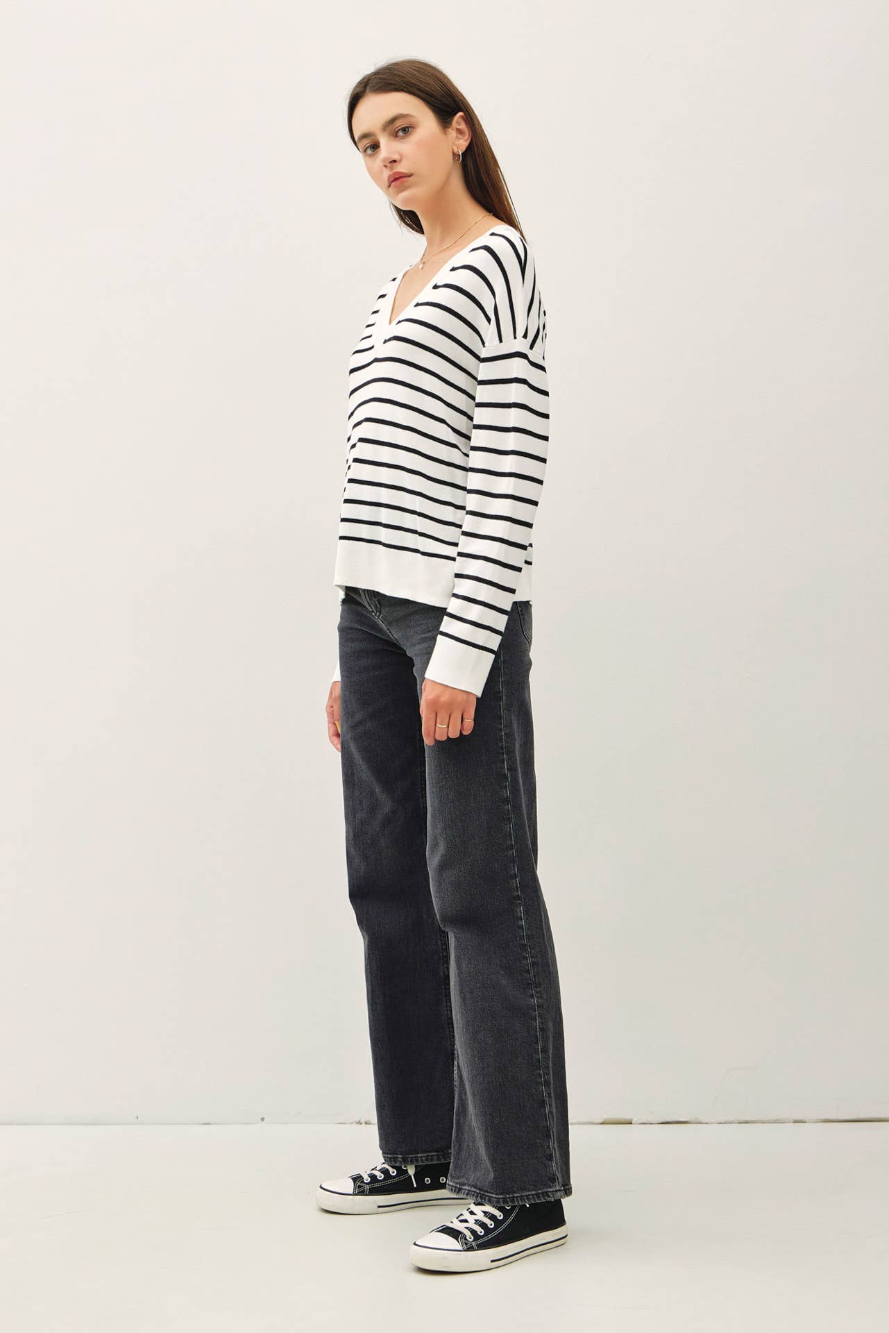 Person wearing a black and white striped sweater with dark jeans on a white background