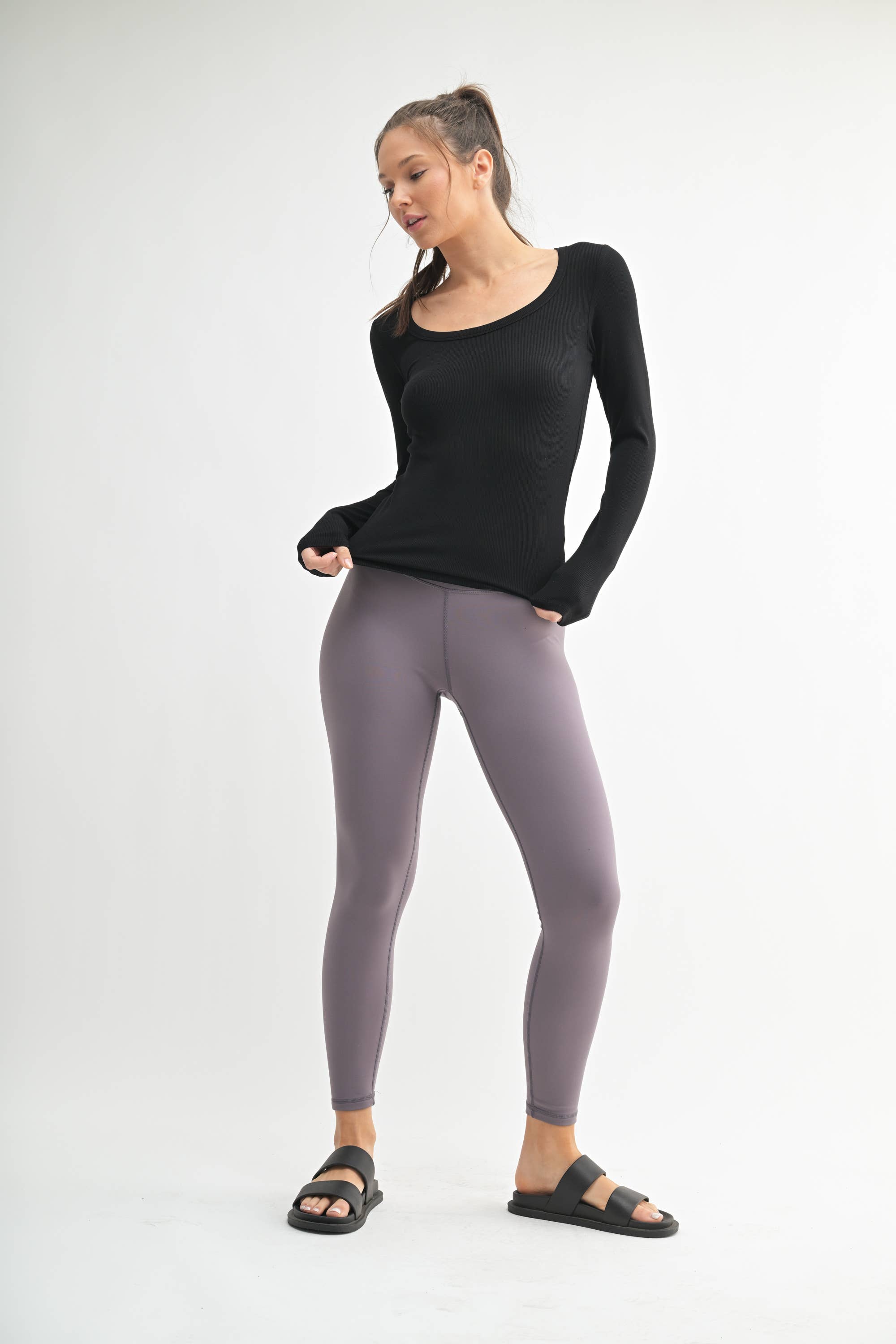 Woman wearing a black long-sleeve top and gray leggings on a white background