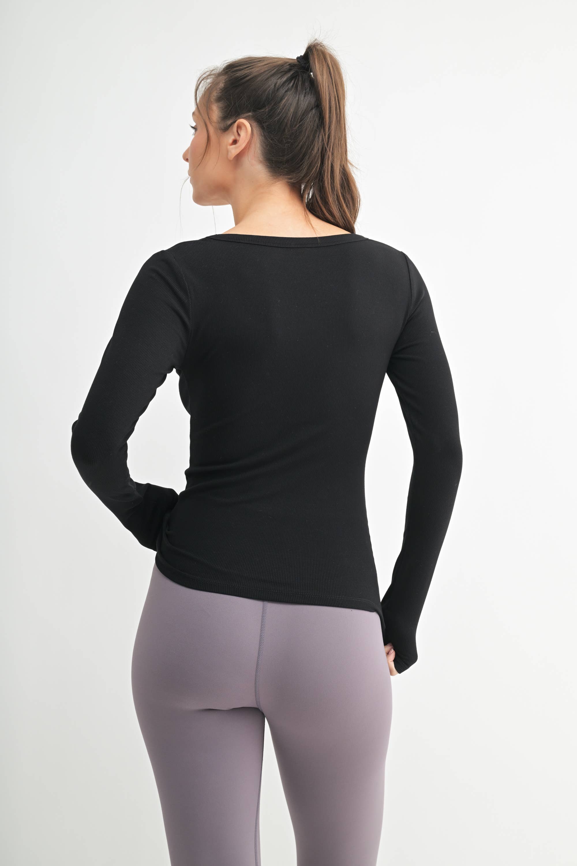 Woman wearing a black long-sleeve top and gray leggings on a white background
