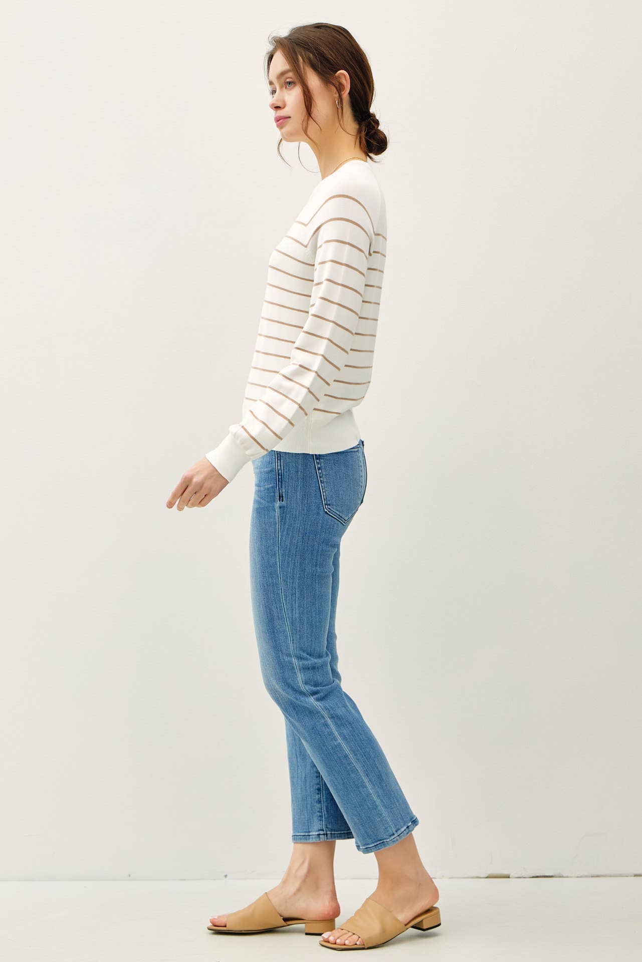 Woman wearing a striped sweater and blue jeans against a white background