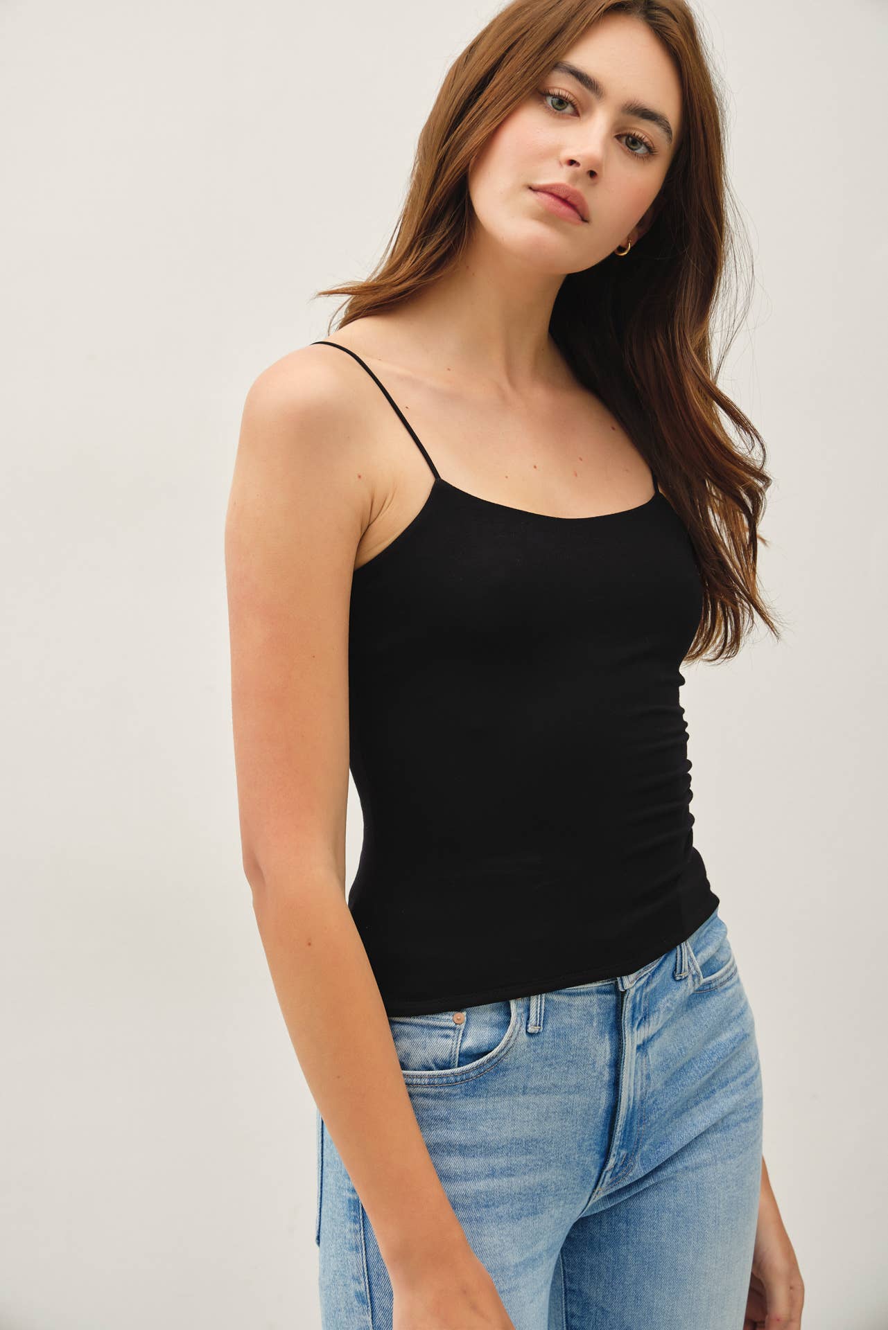 Woman wearing a black tank top and blue jeans against a plain background