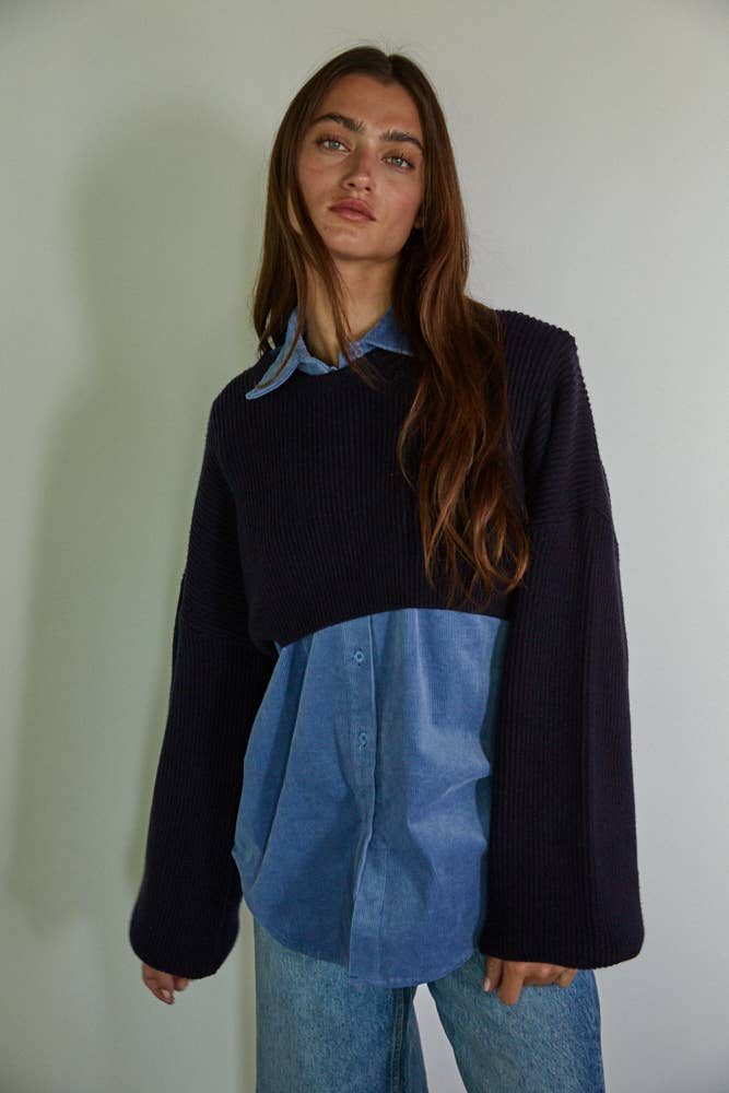 Person wearing a dark sweater over a blue shirt with a plain background