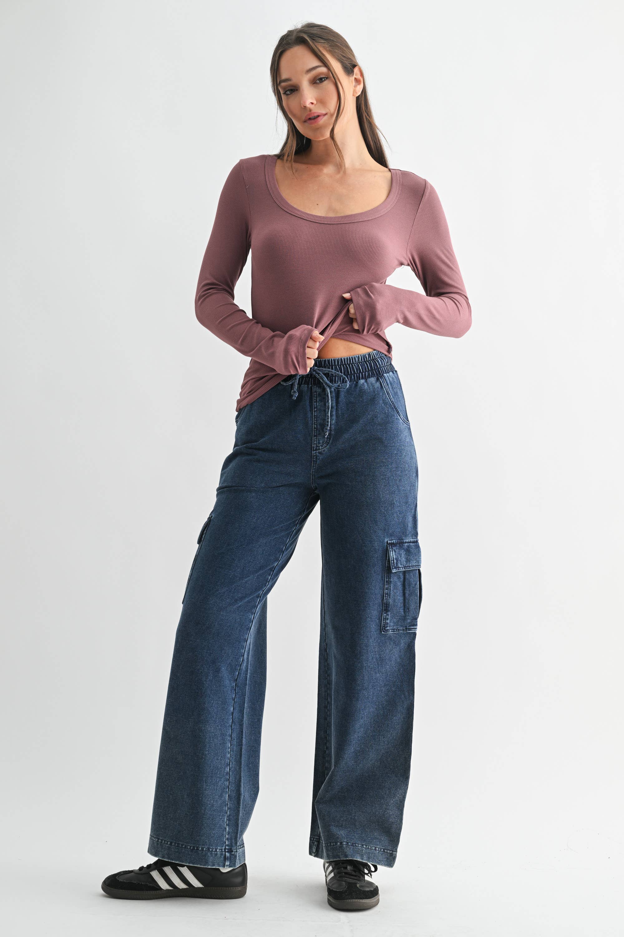Woman wearing a mauve long-sleeve top and blue cargo pants on a white background