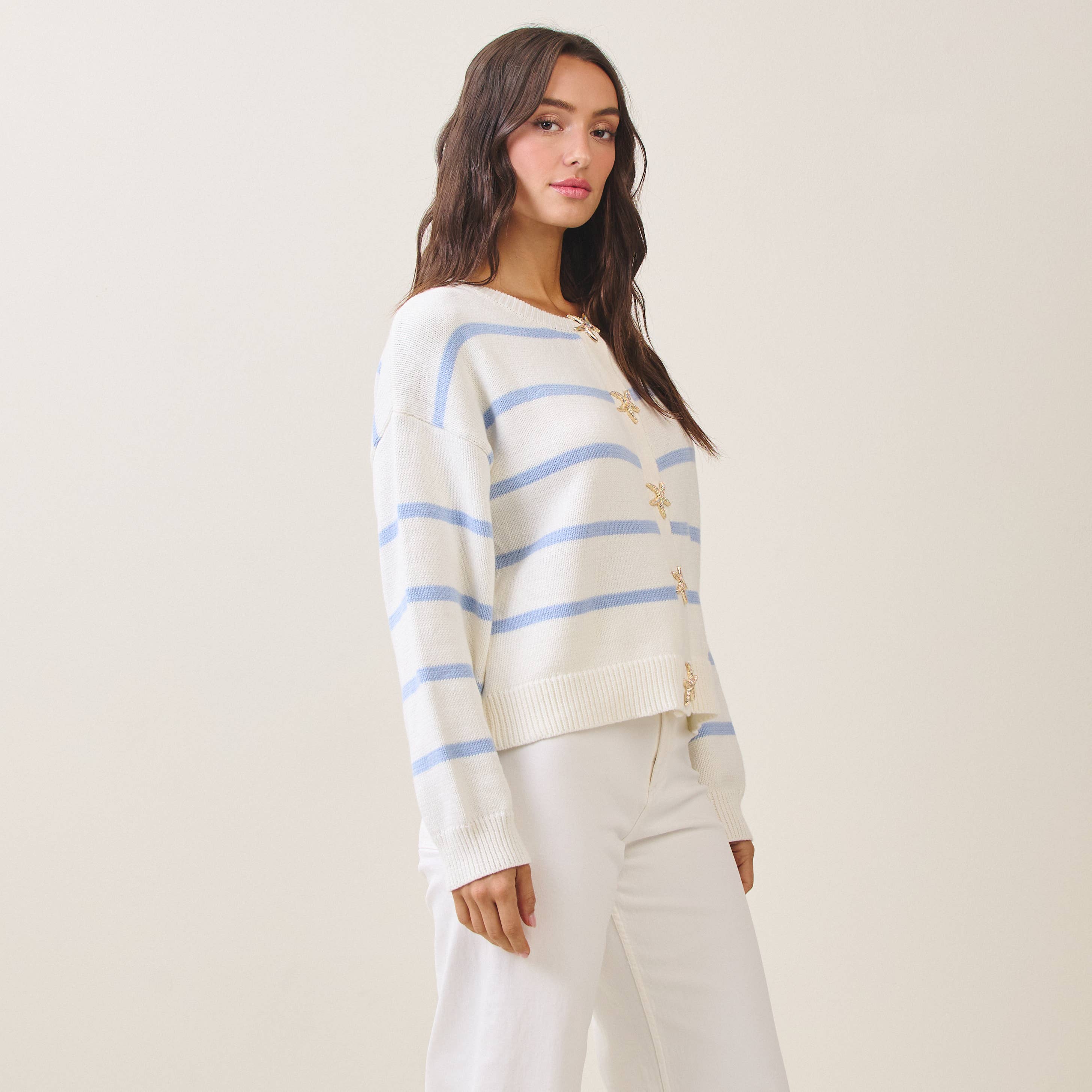 Woman wearing a striped sweater and white pants against a plain background