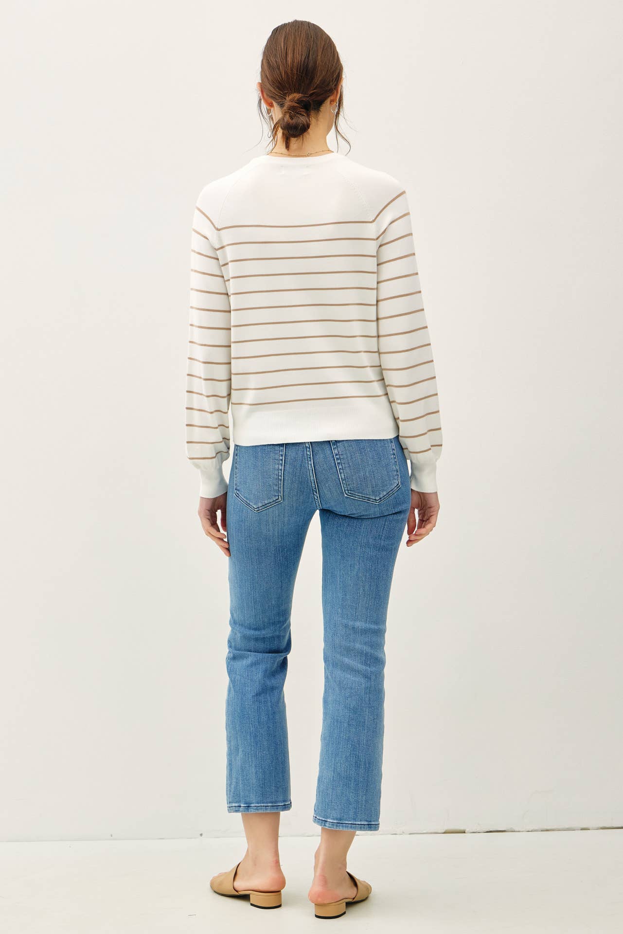 Person wearing a striped sweater and blue jeans on a plain background