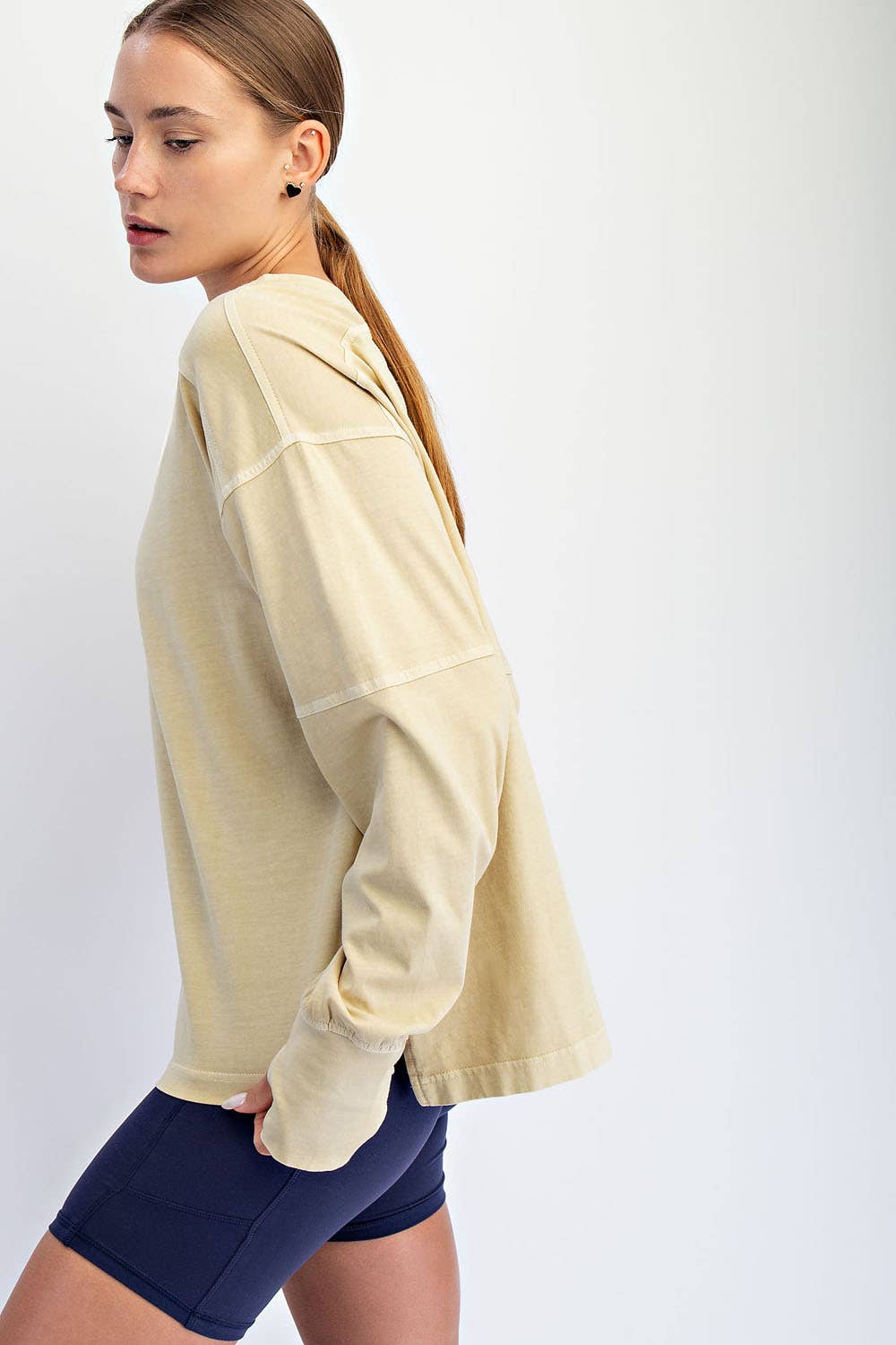 Woman wearing a beige long-sleeve top and navy shorts on a white background