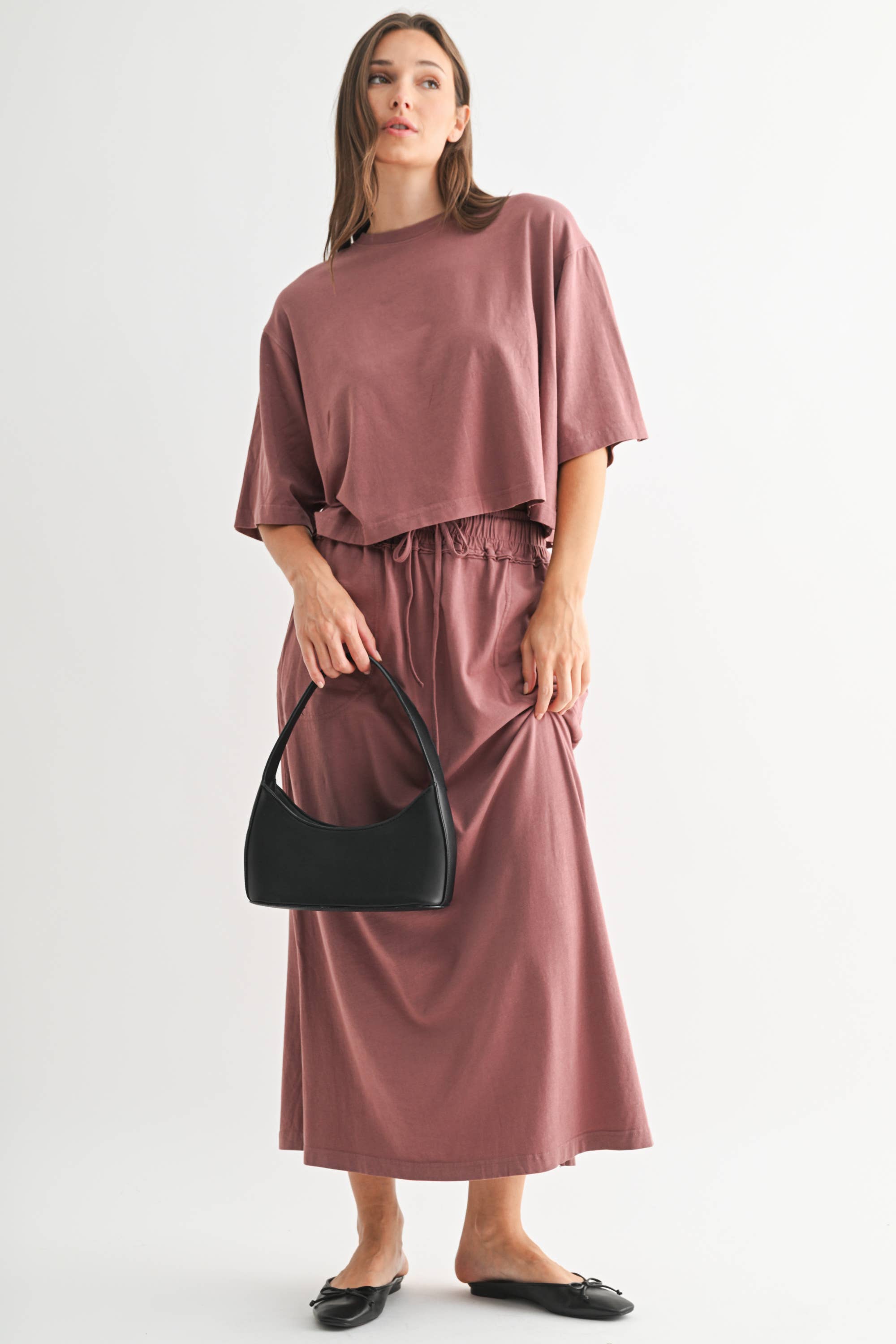 Woman wearing a mauve dress holding a black handbag on a white background