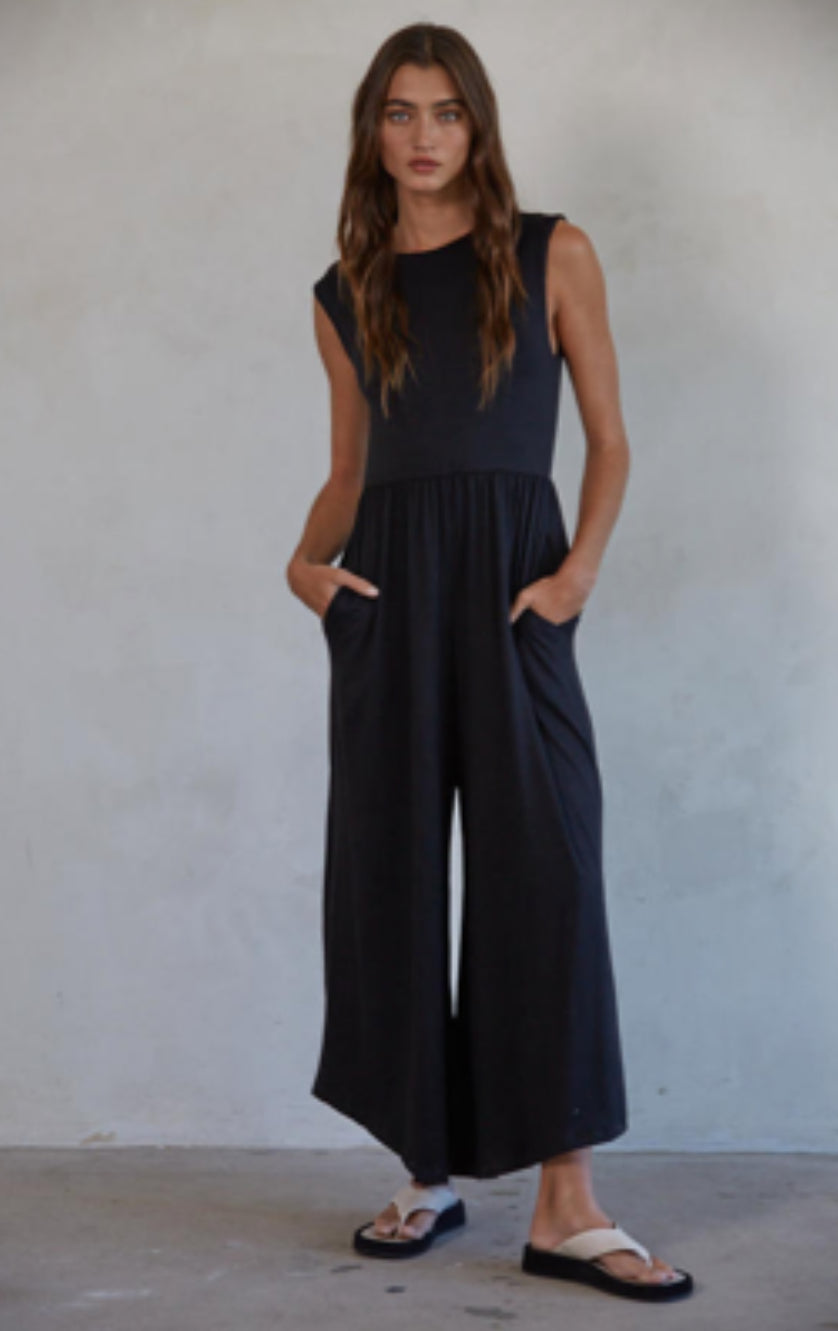 Woman wearing a black sleeveless jumpsuit against a plain background