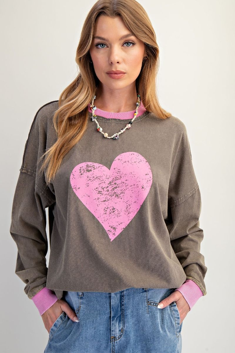 Woman wearing a brown sweatshirt with a pink heart design on a plain background