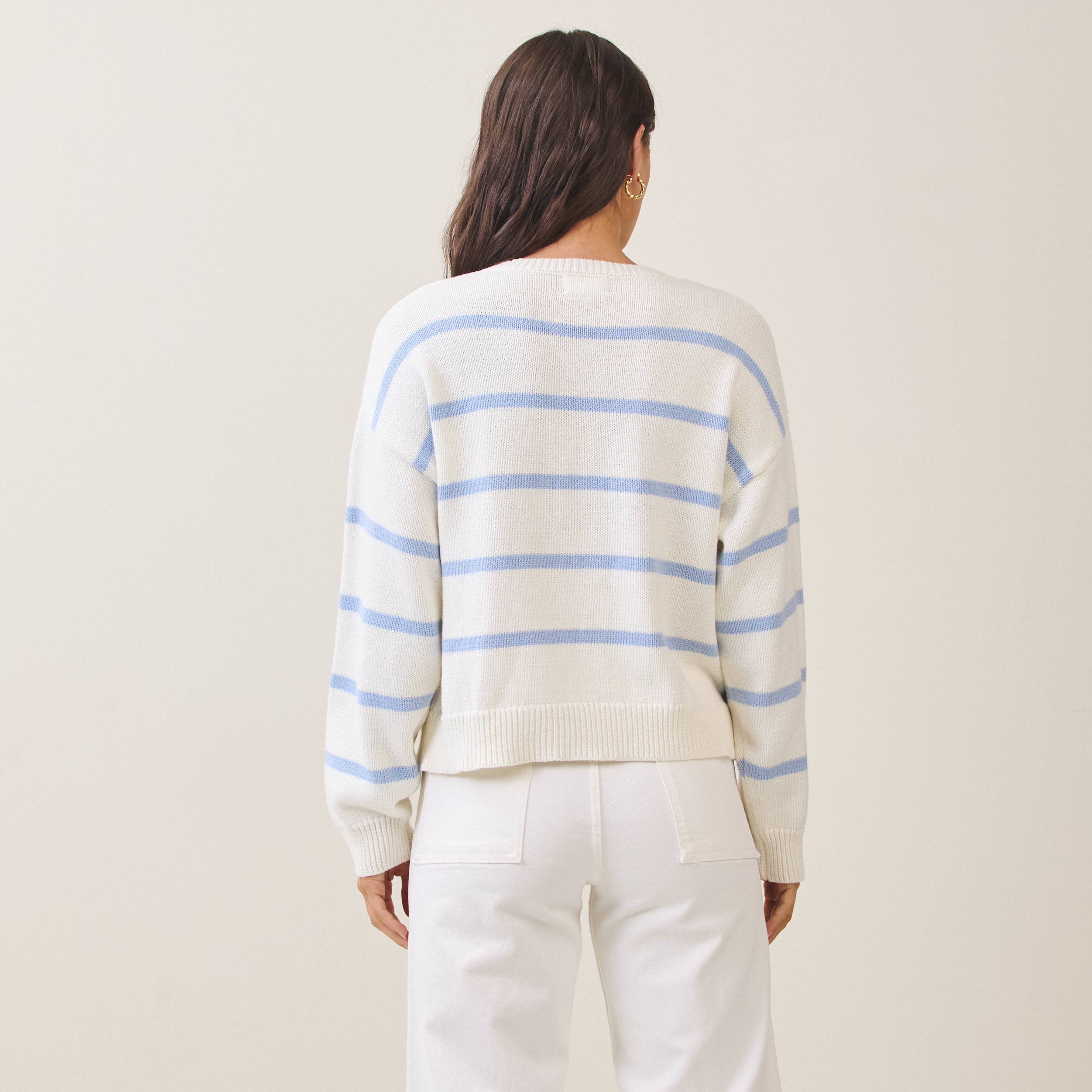 Person wearing a white sweater with blue stripes and white pants on a beige background