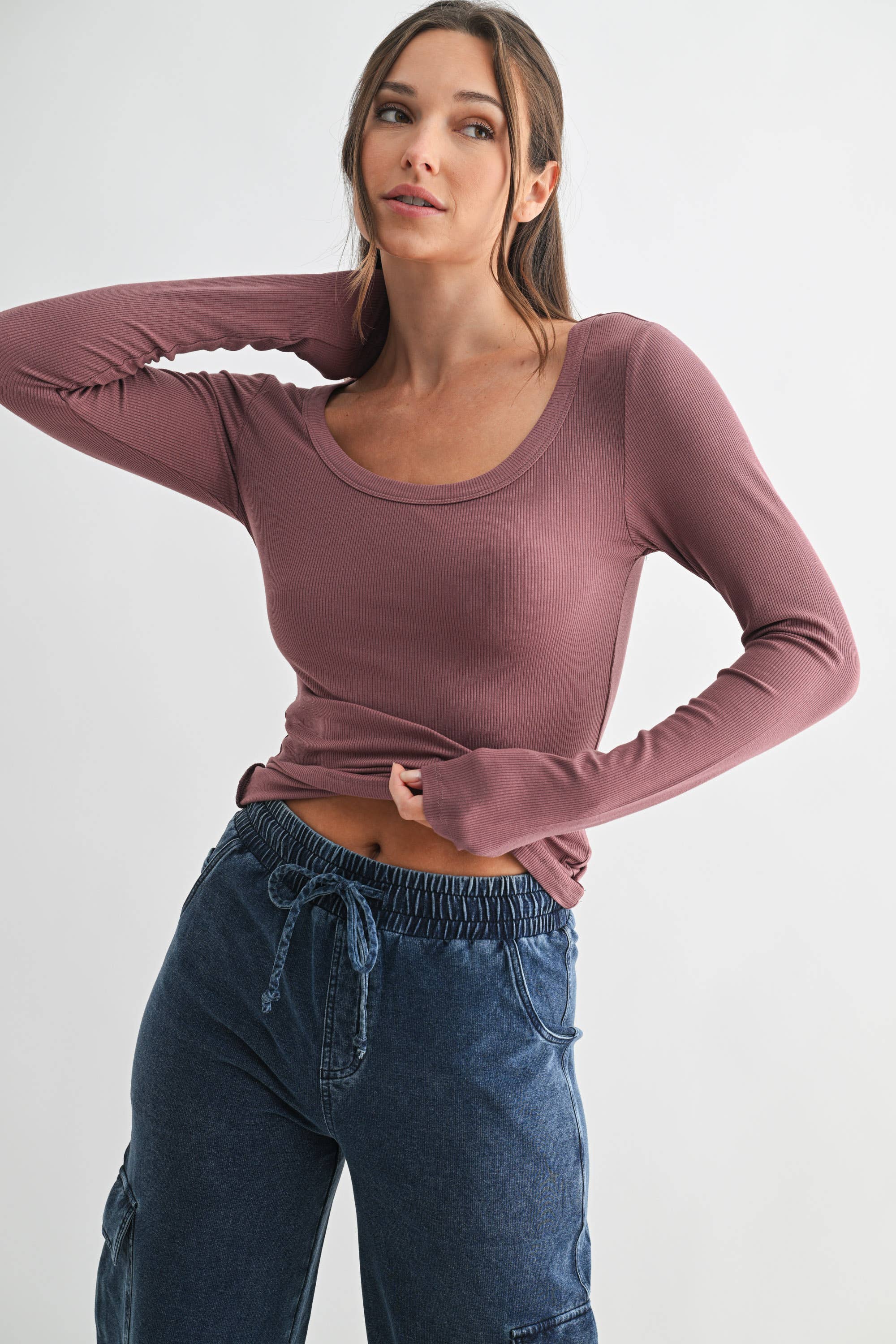 Woman wearing a mauve long-sleeve top and blue jeans on a white background