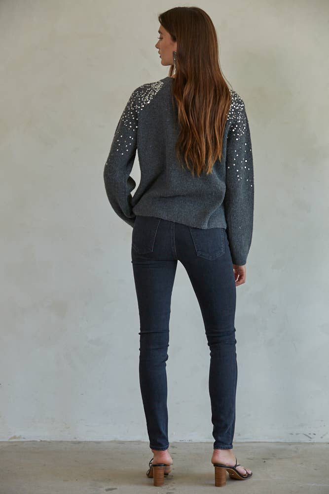 Woman wearing a gray blazer with sequin details on the back against a plain wall.