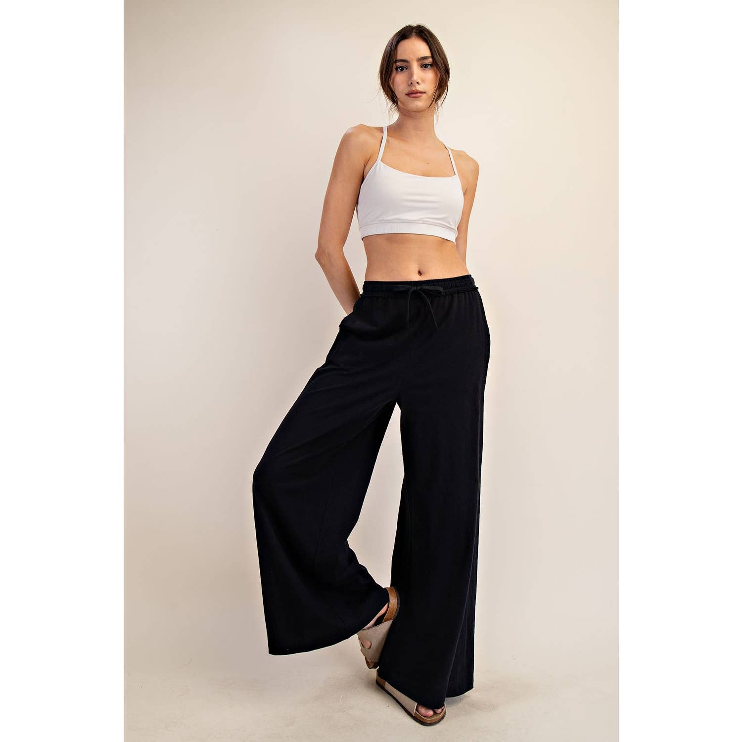 Woman wearing a white top and black wide-leg pants against a plain background