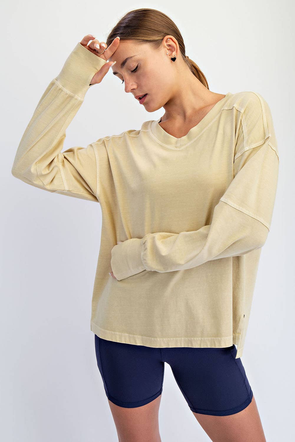 Woman wearing a beige long-sleeve top and navy shorts on a white background