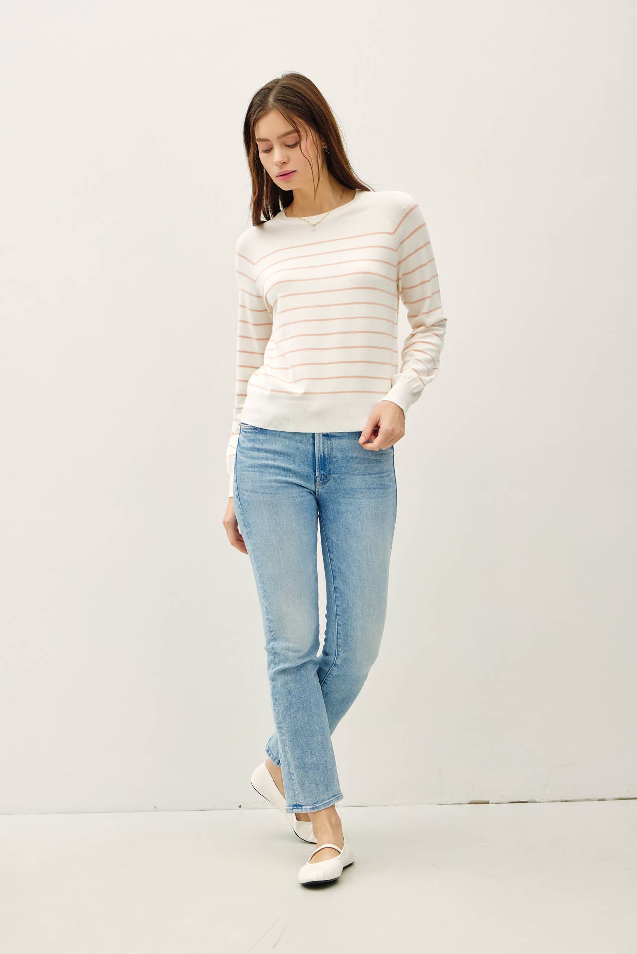 Woman wearing a striped sweater and light blue jeans against a white background