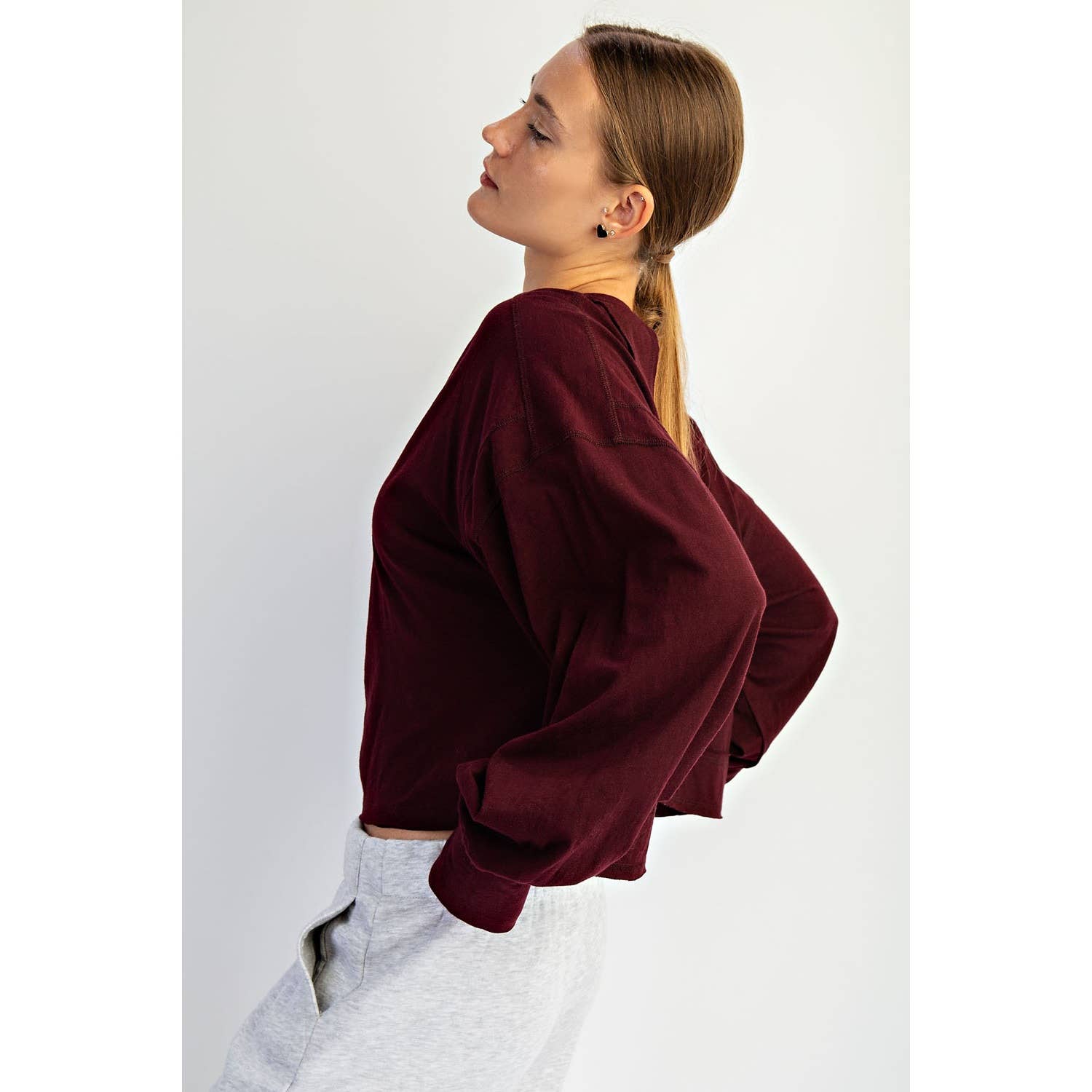 Woman wearing a burgundy sweater and light gray pants against a white background