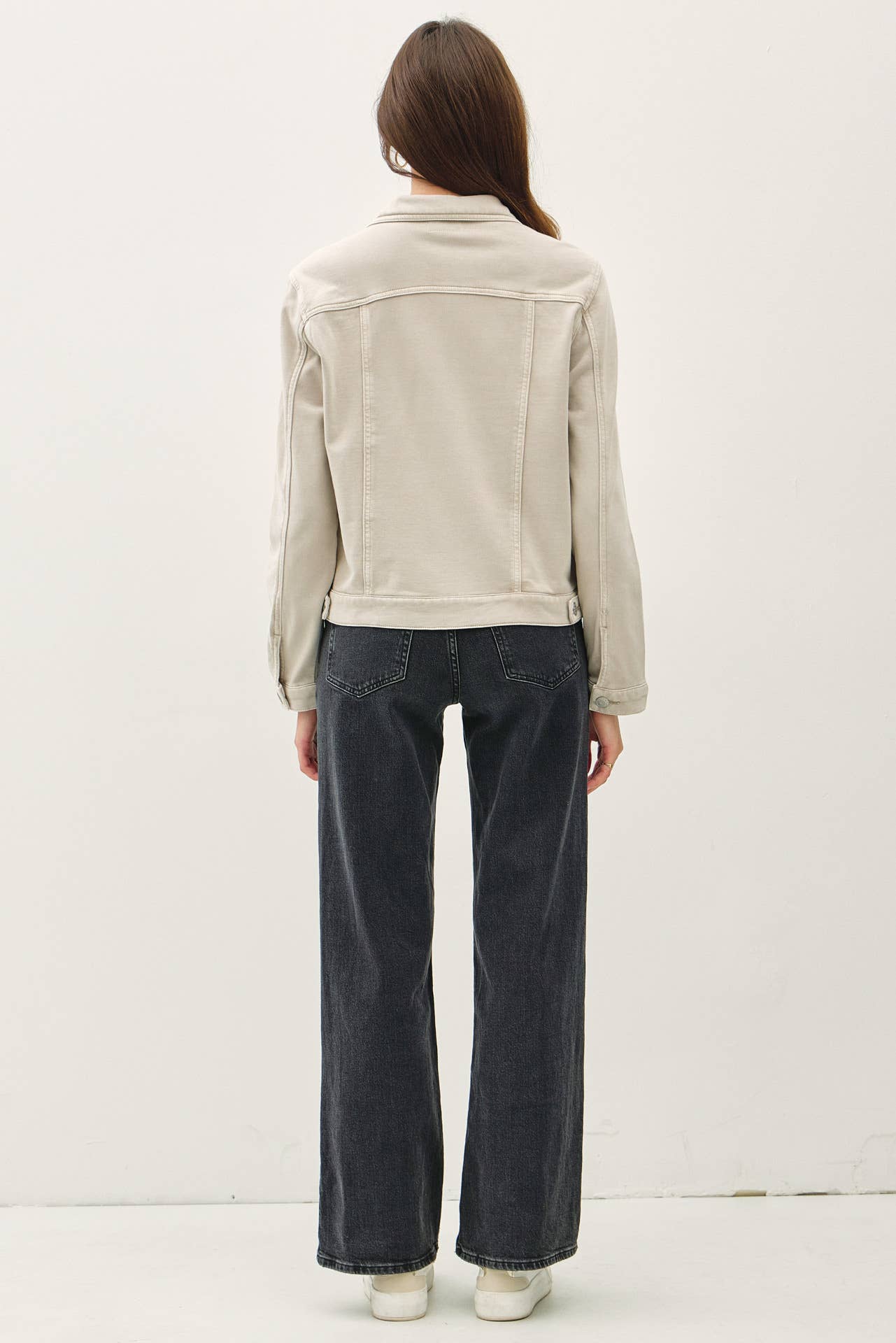 Person wearing a beige jacket and dark jeans on a white background