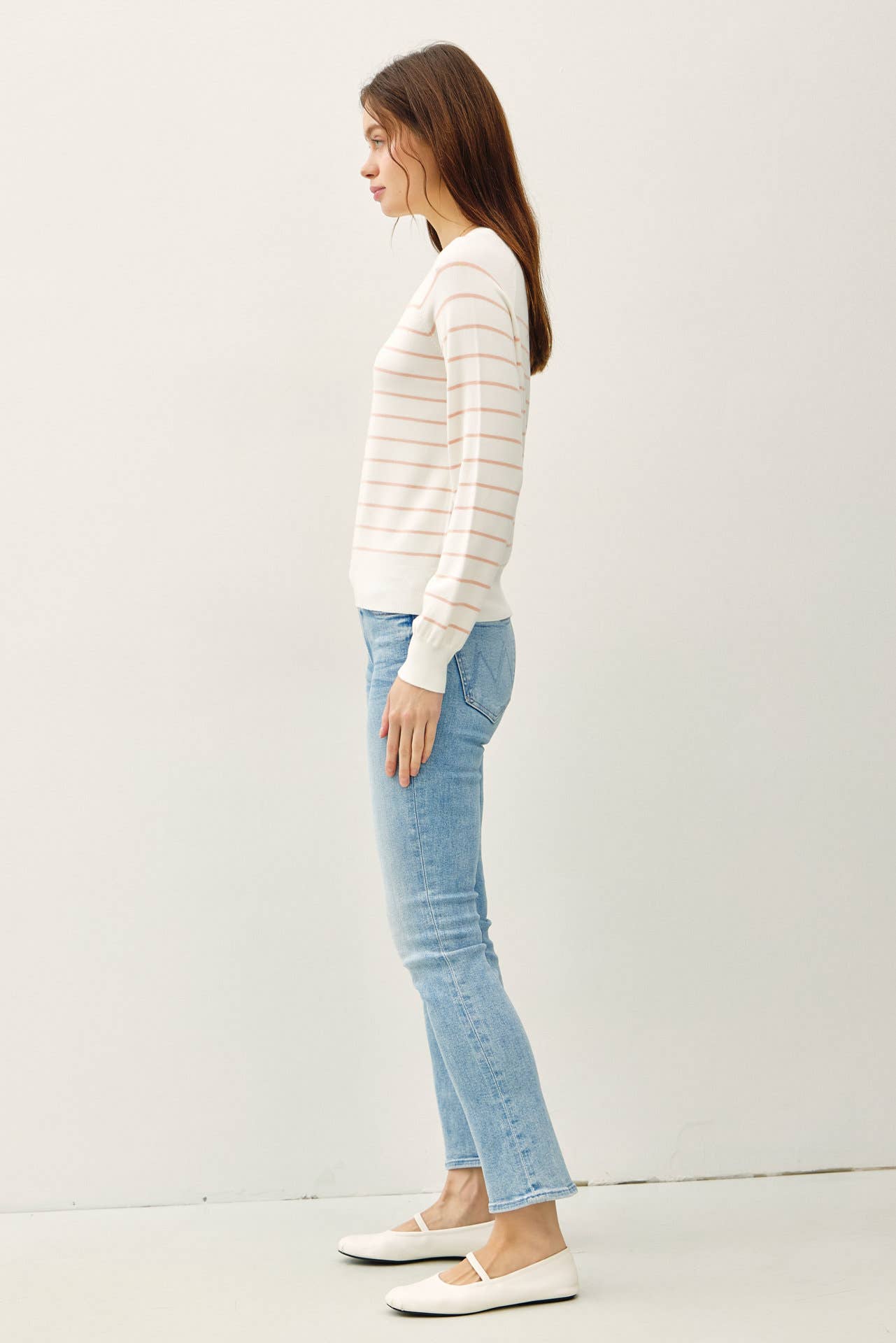 Woman wearing a striped sweater and light blue jeans against a white background