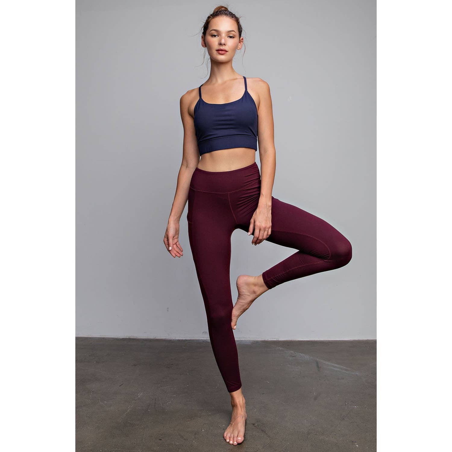 Woman wearing a blue sports bra and maroon leggings posing against a gray background