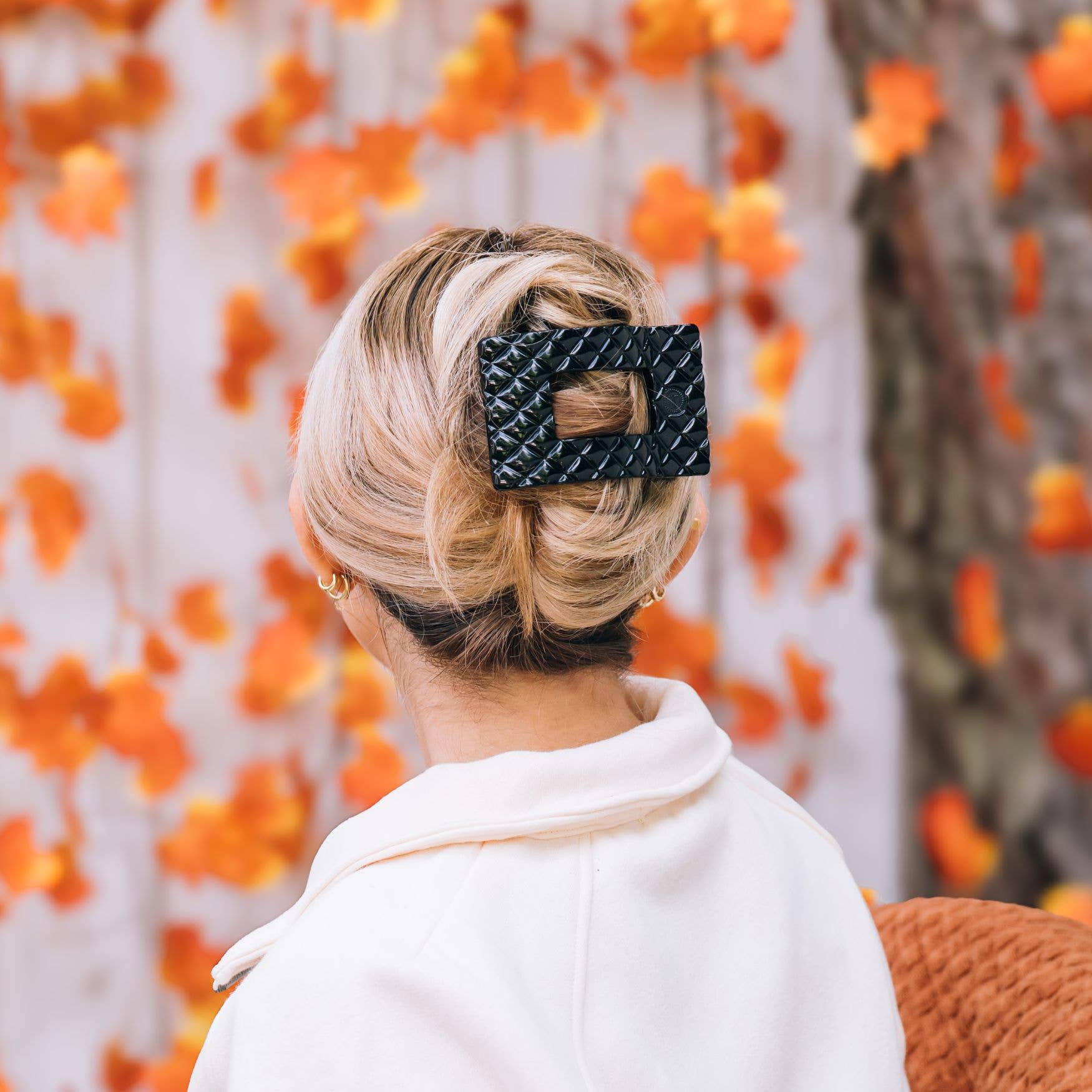 Person with styled hair wearing a black hair clip against an orange floral background